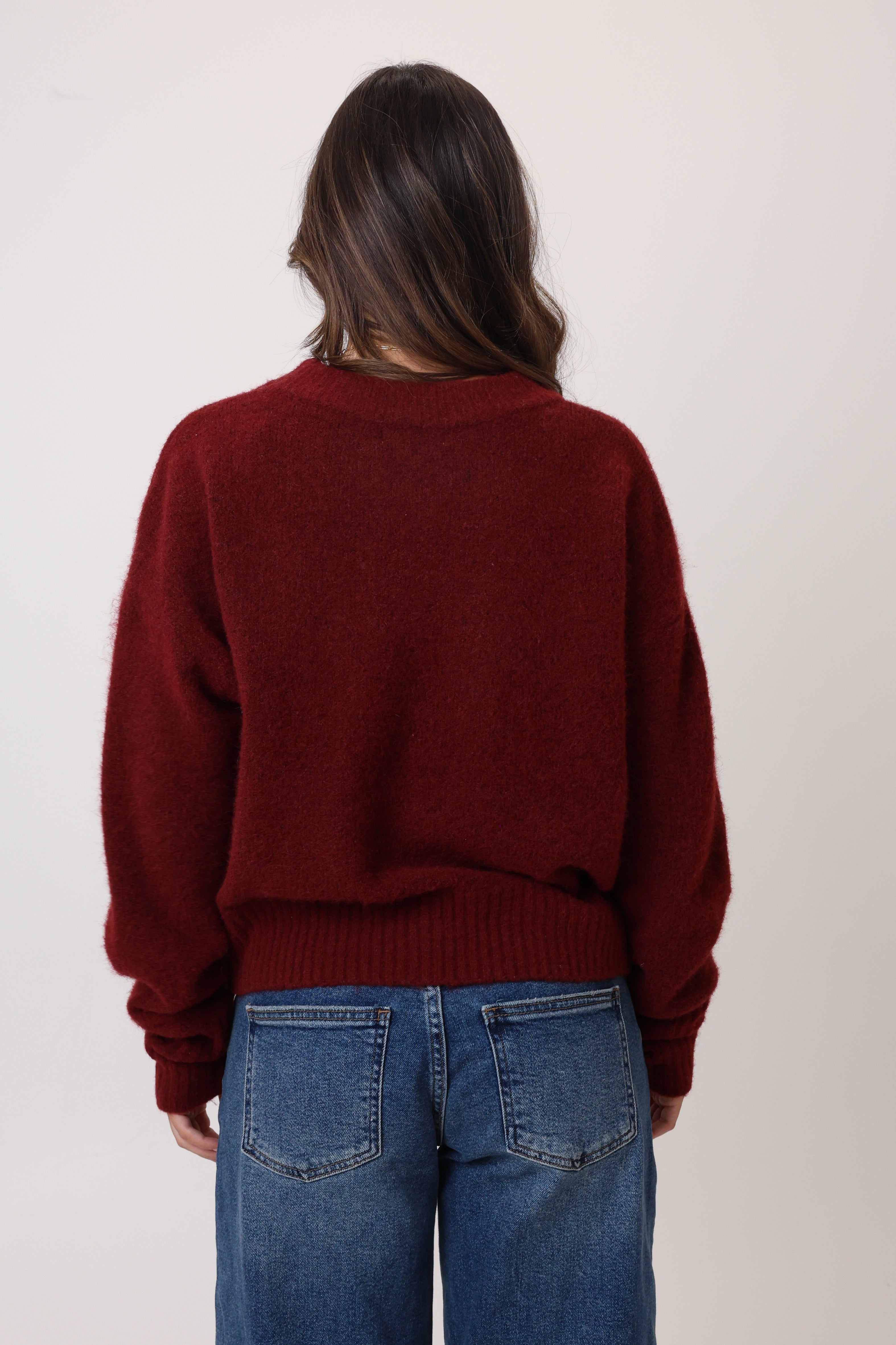 Person wearing a burgundy sweater and blue jeans against a plain background