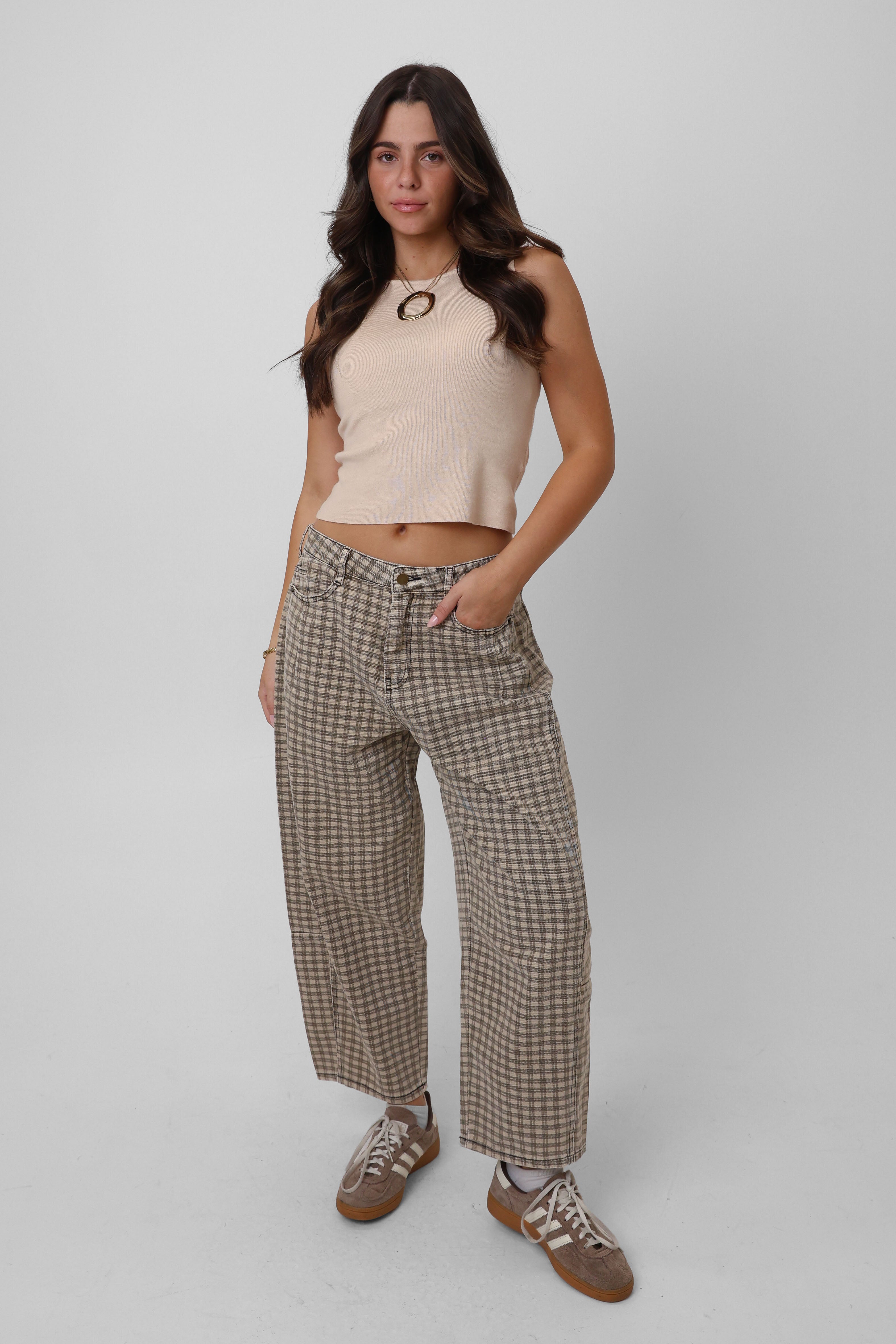 Woman wearing a beige sleeveless top and plaid pants on a white background