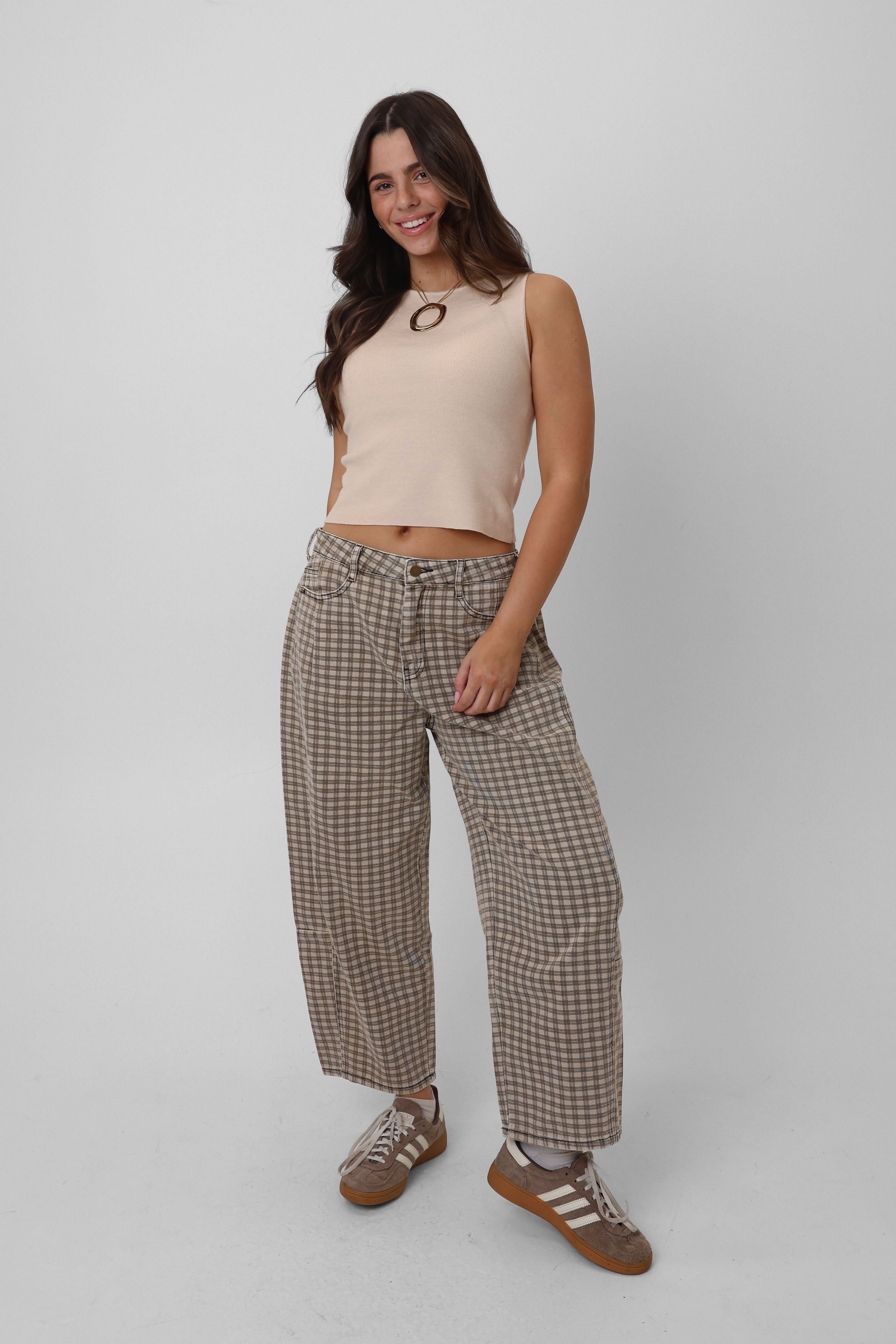 Woman wearing a beige sleeveless top and checkered pants on a white background