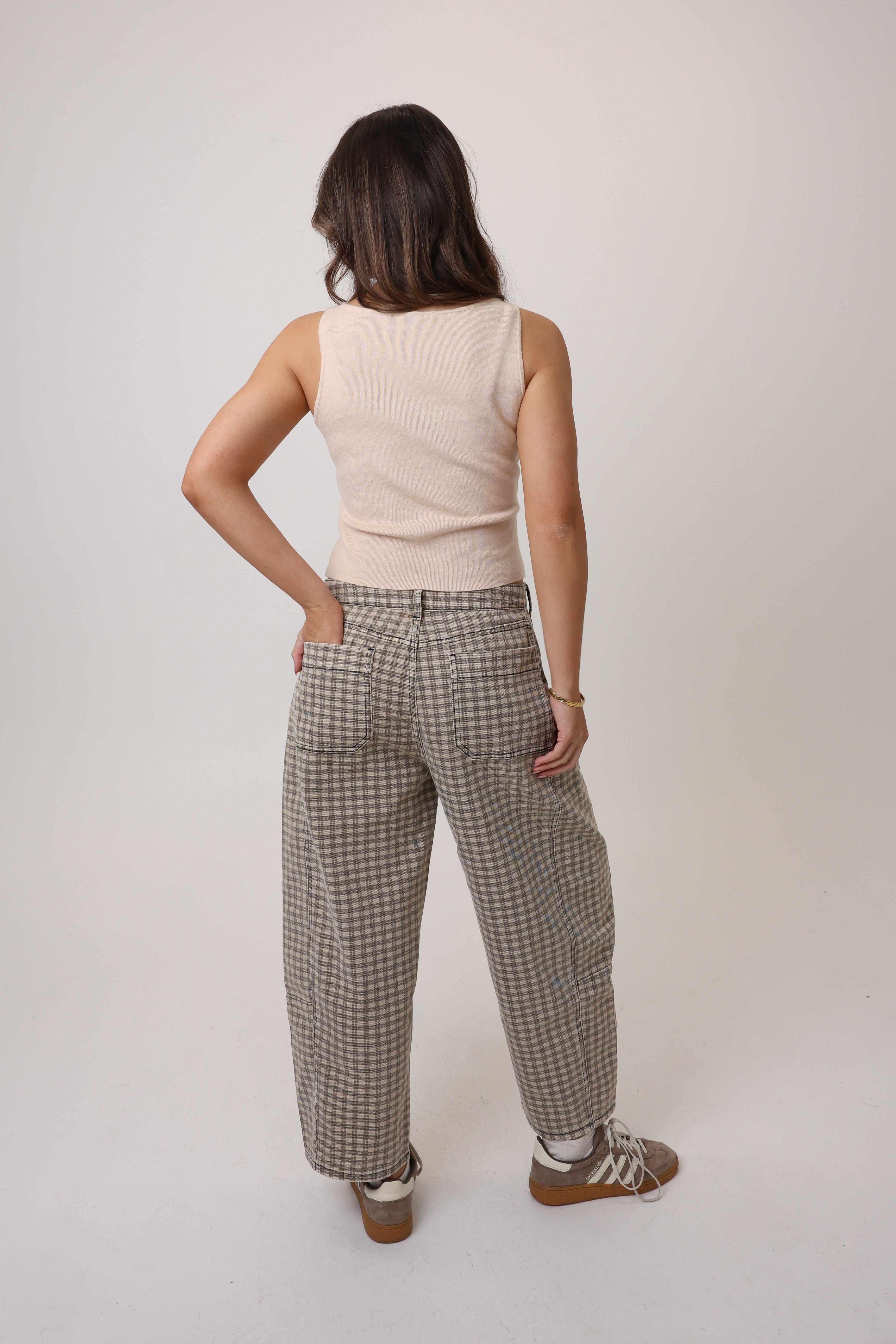 Person wearing a beige sleeveless top and checkered pants on a white background