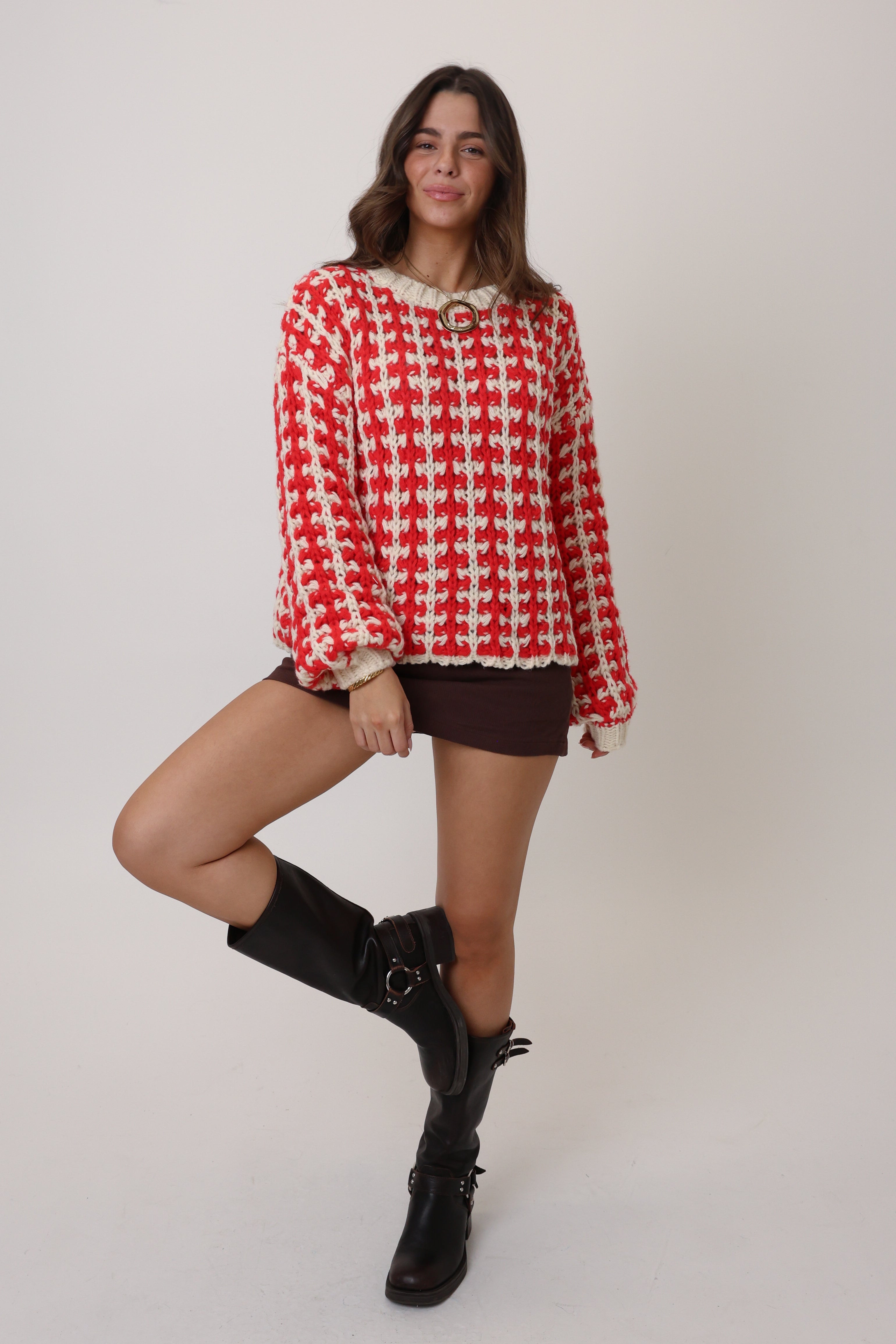 Woman wearing a red and white checkered sweater with black boots on a plain background