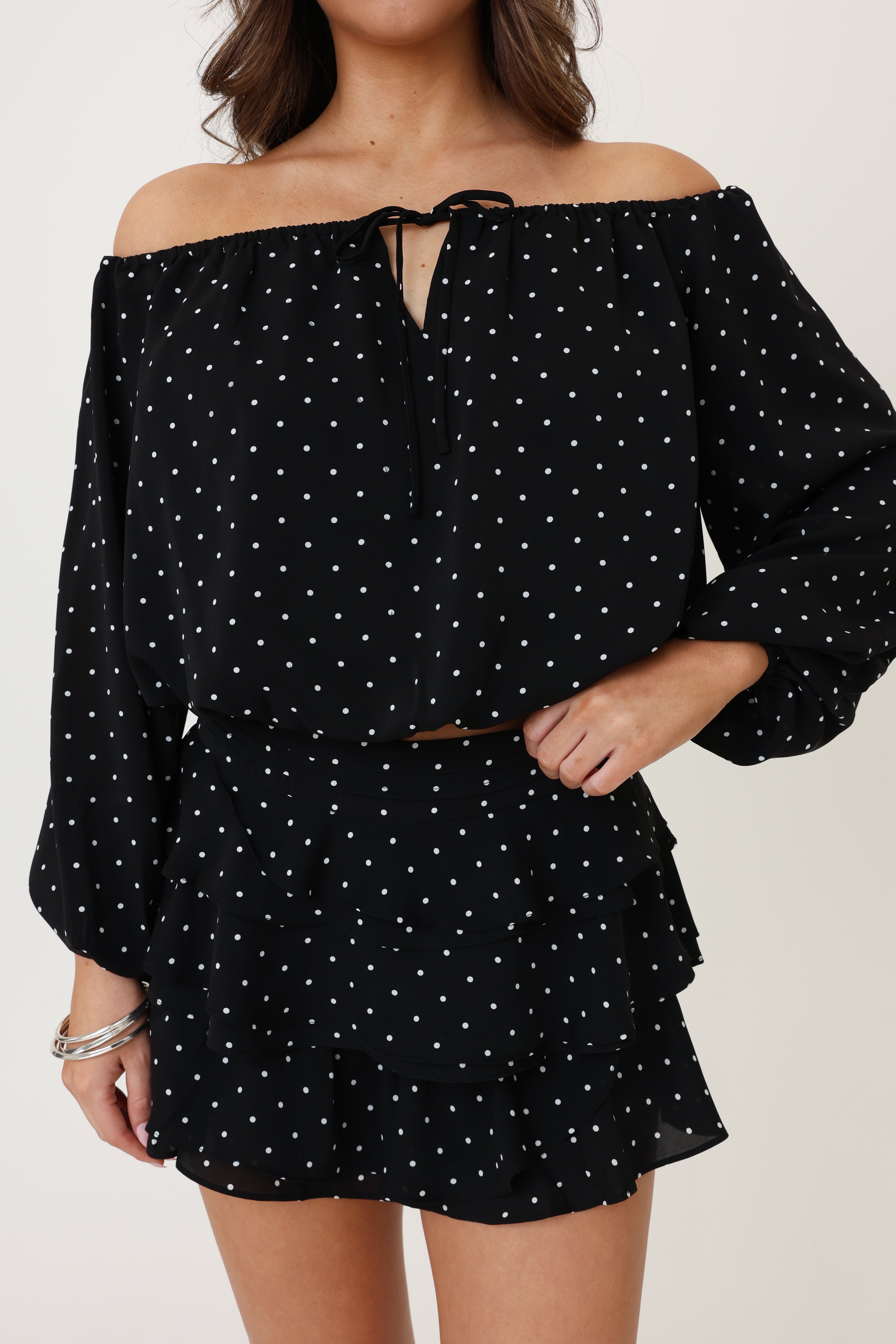 Black polka dot off-shoulder dress worn by a person on a plain background
