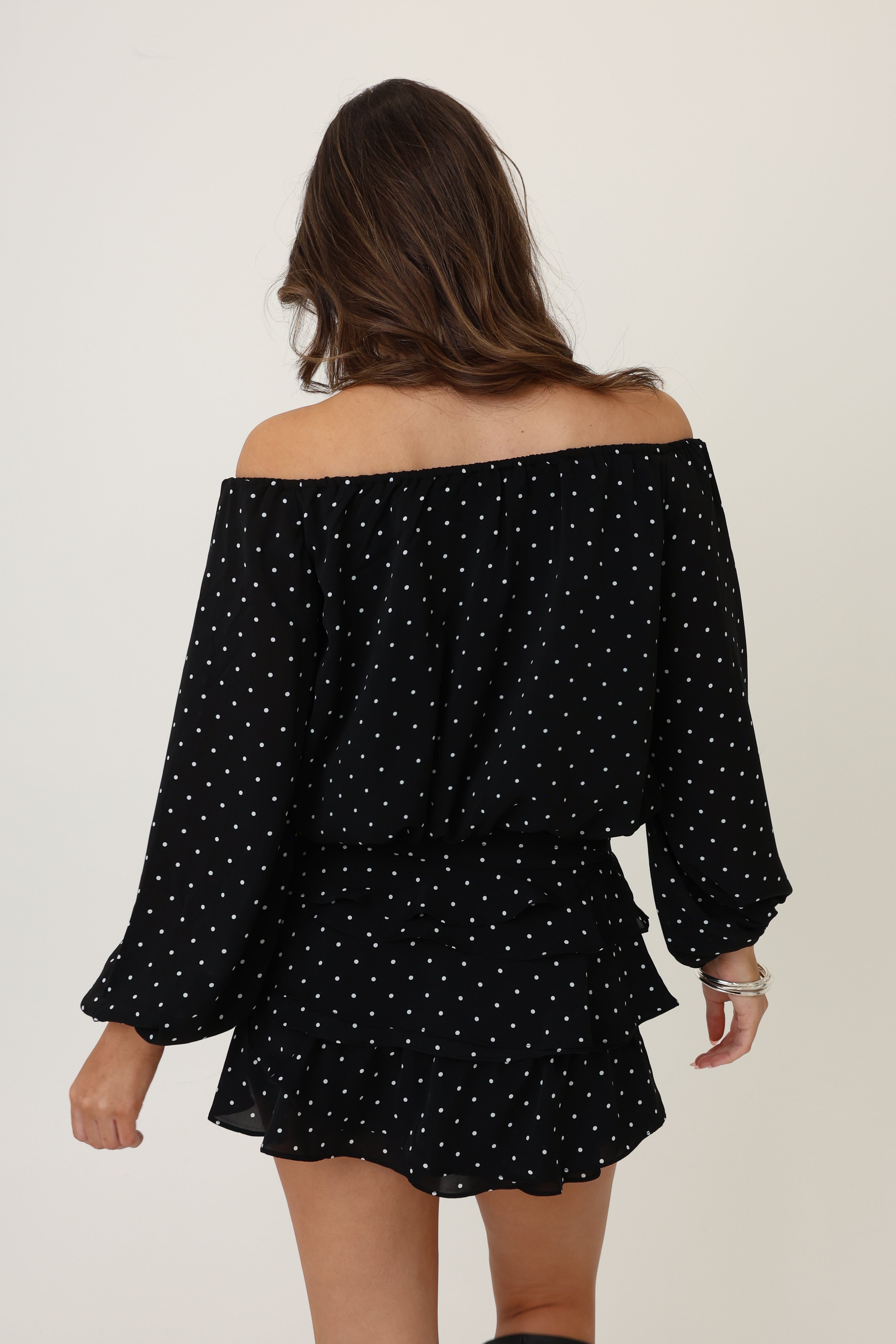 Woman wearing a black off-shoulder dress with white polka dots on a plain background