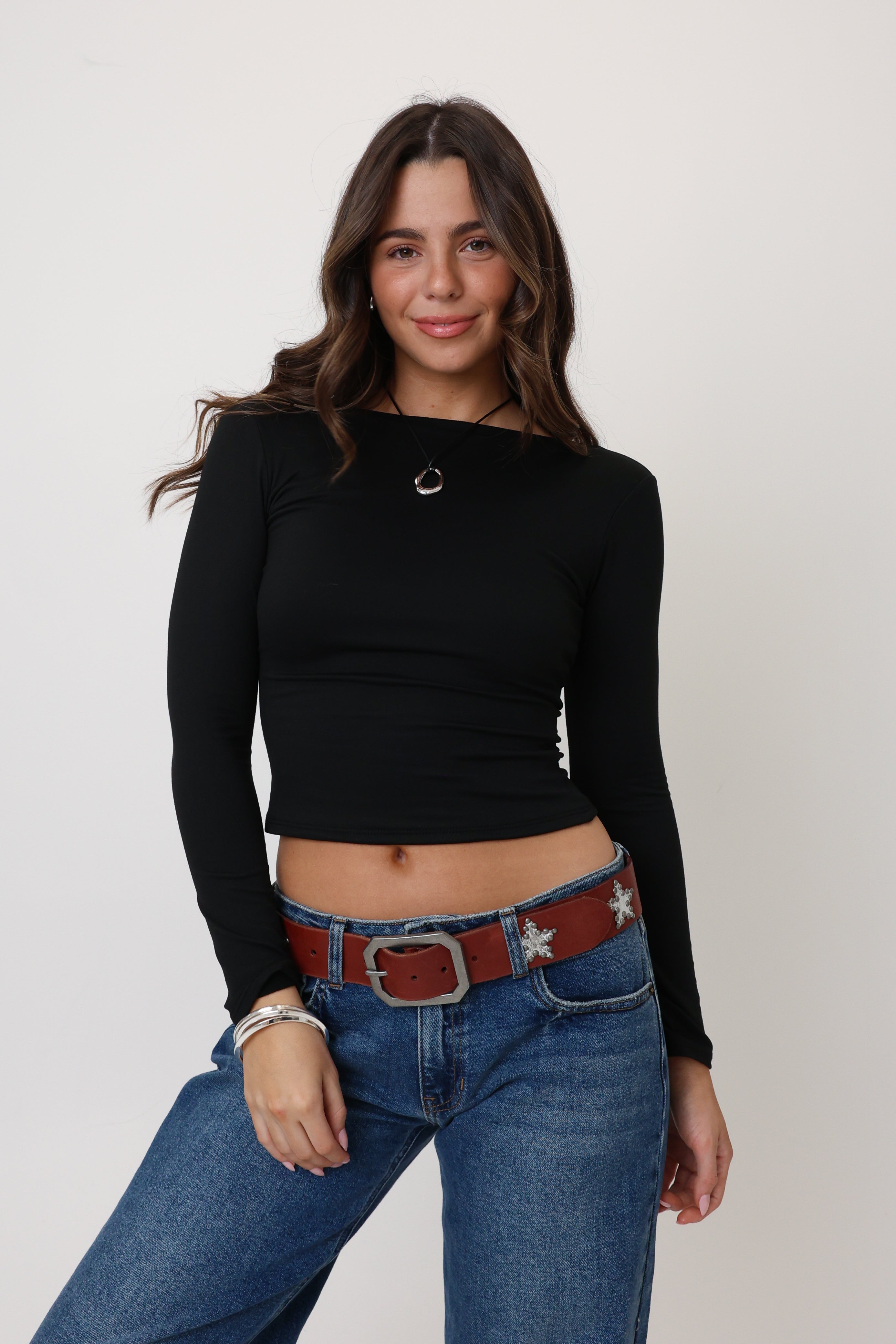 Woman wearing a black long-sleeve top and blue jeans with a red belt on a white background