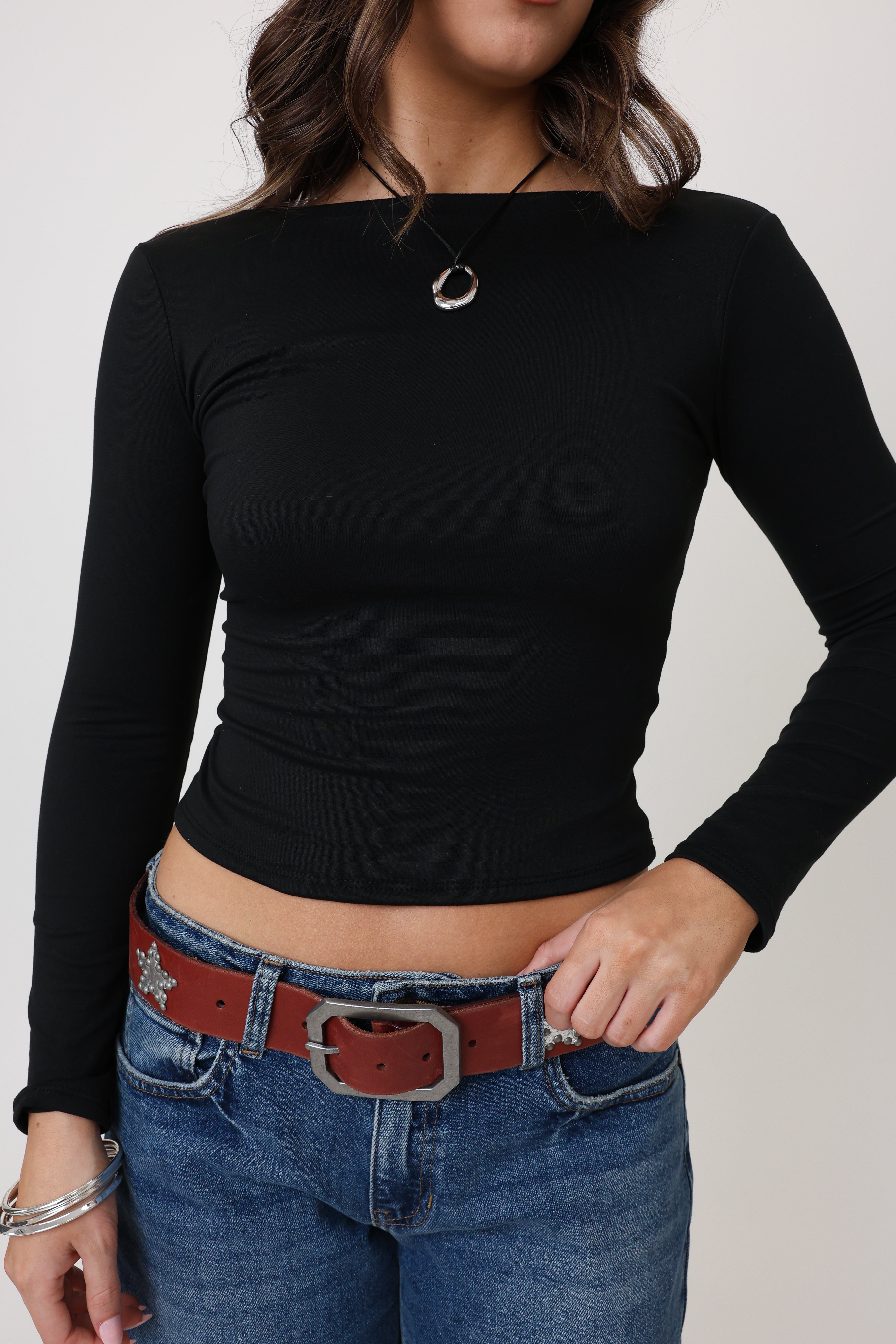 Person wearing a black long-sleeve top and blue jeans with a red belt on a plain background