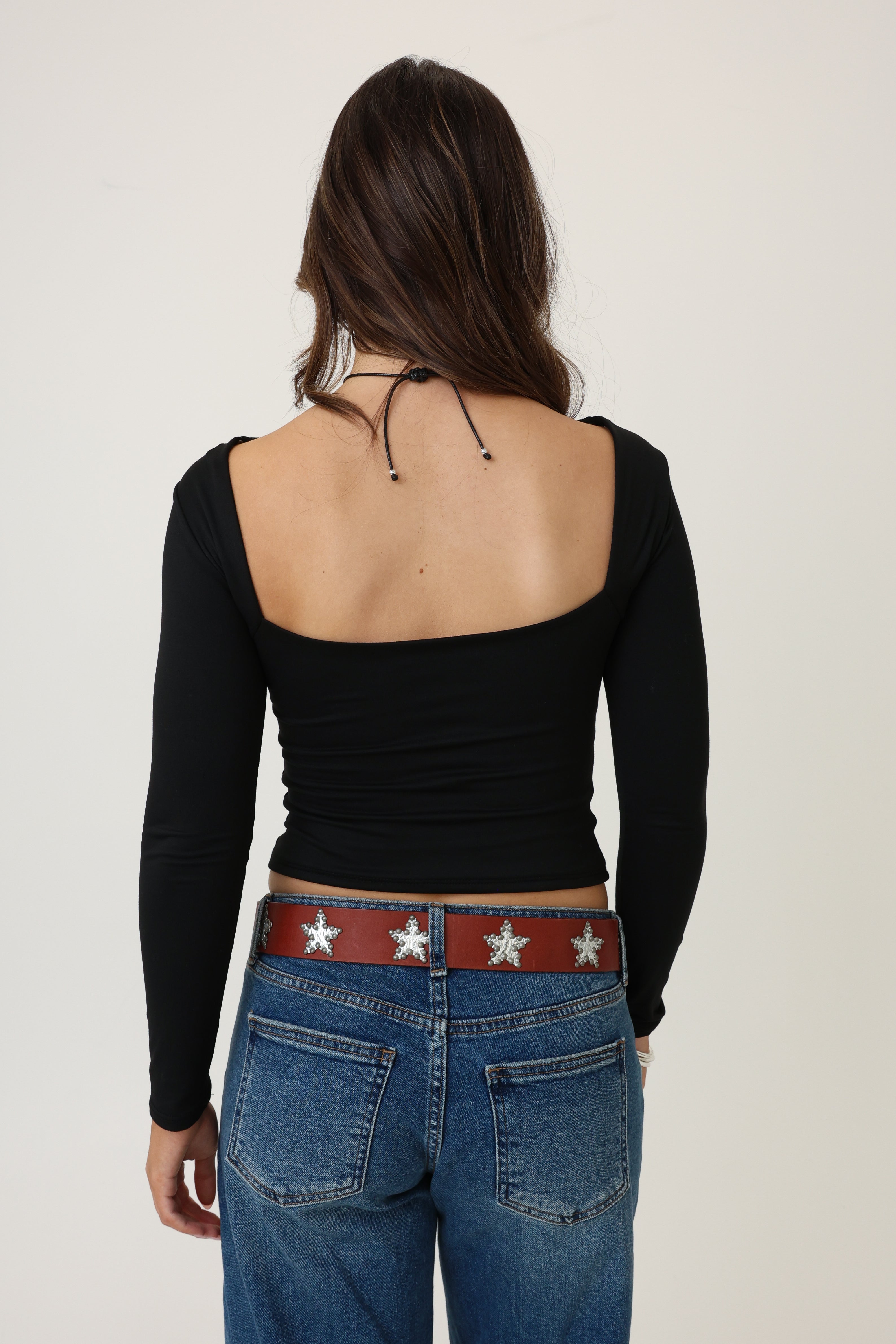 Person wearing a black long-sleeve top and blue jeans with a red belt featuring white stars on a plain background