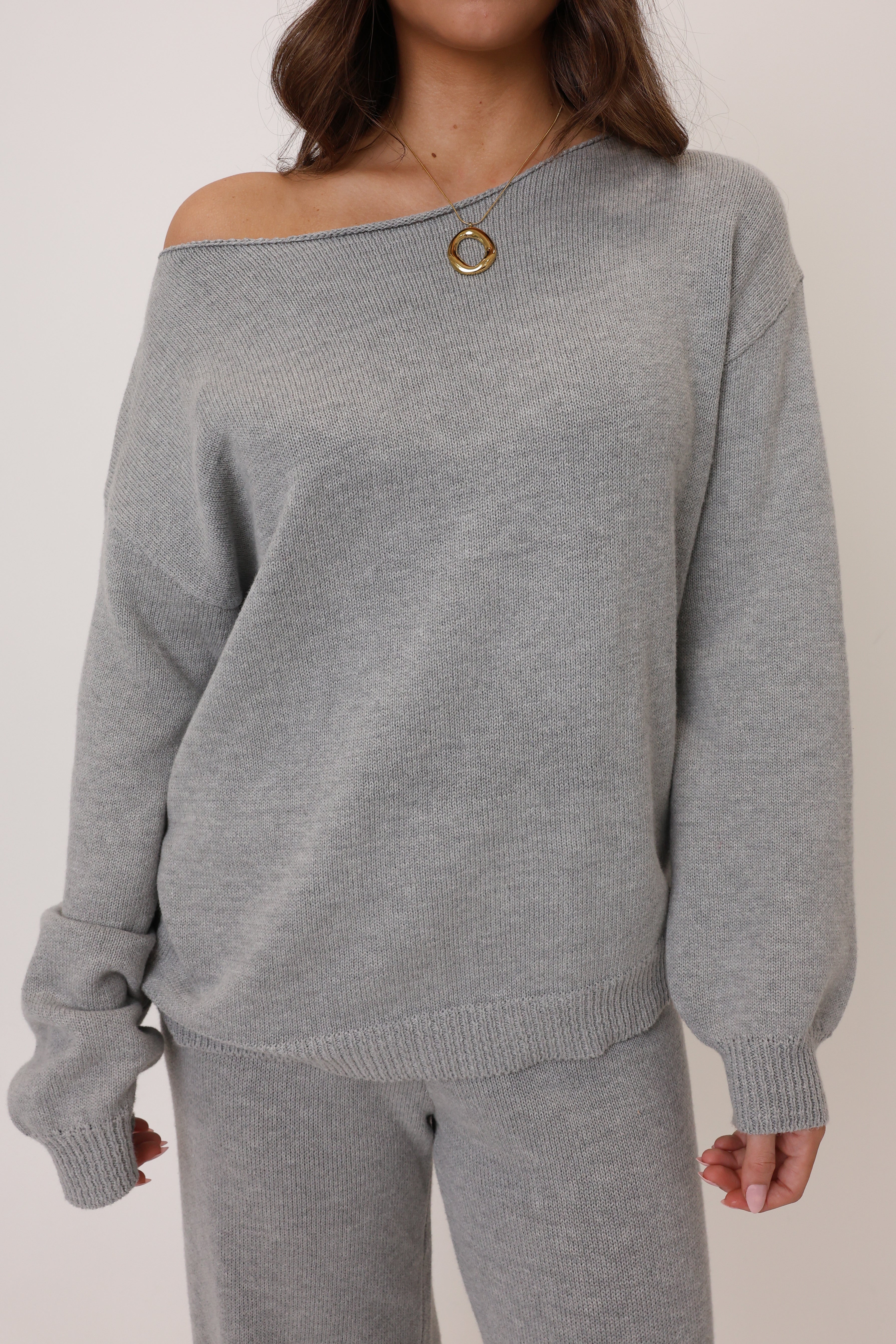 Person wearing a gray off-shoulder sweater and pants on a plain background