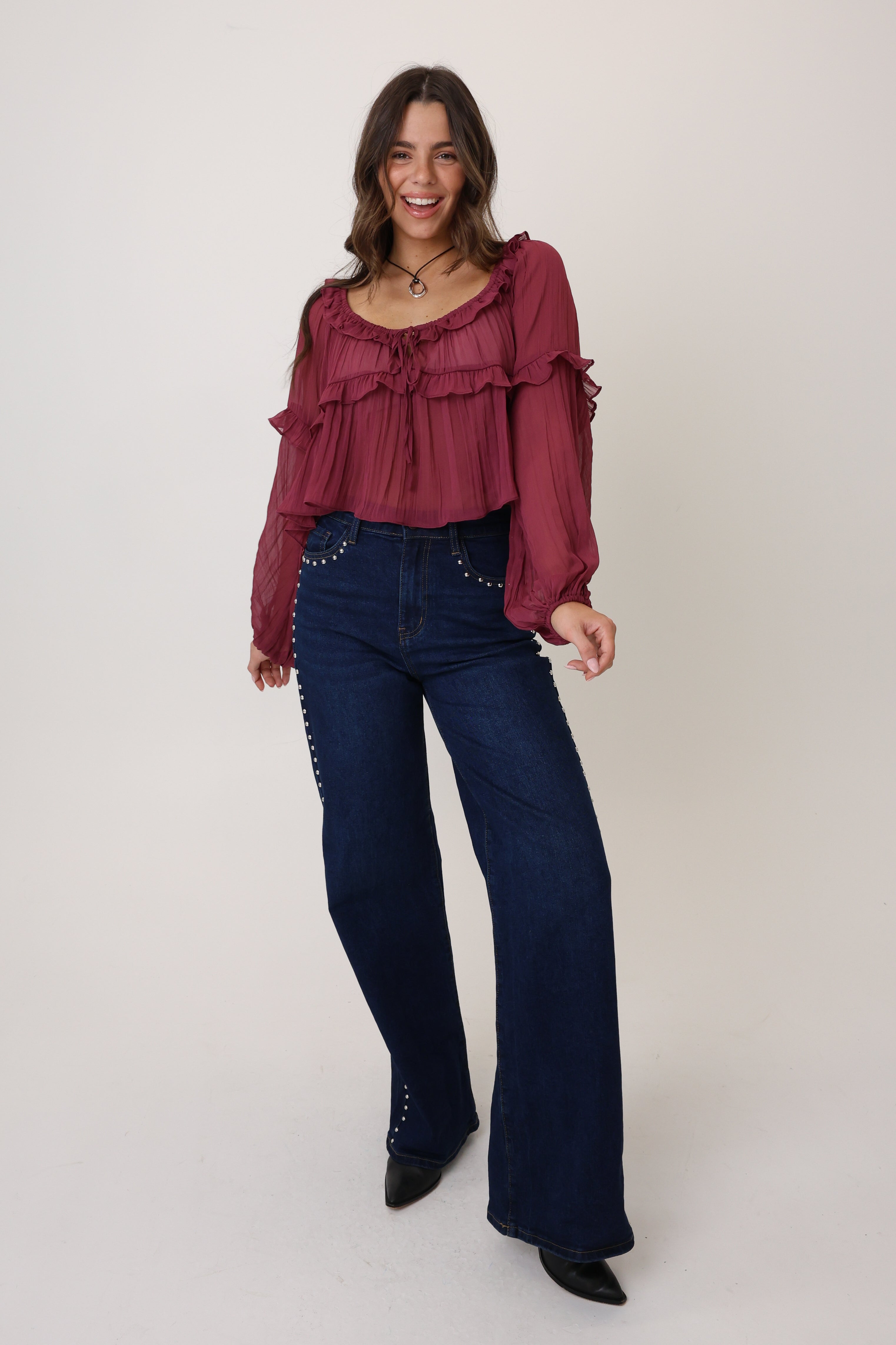 Woman wearing a burgundy ruffled blouse and dark blue jeans on a white background