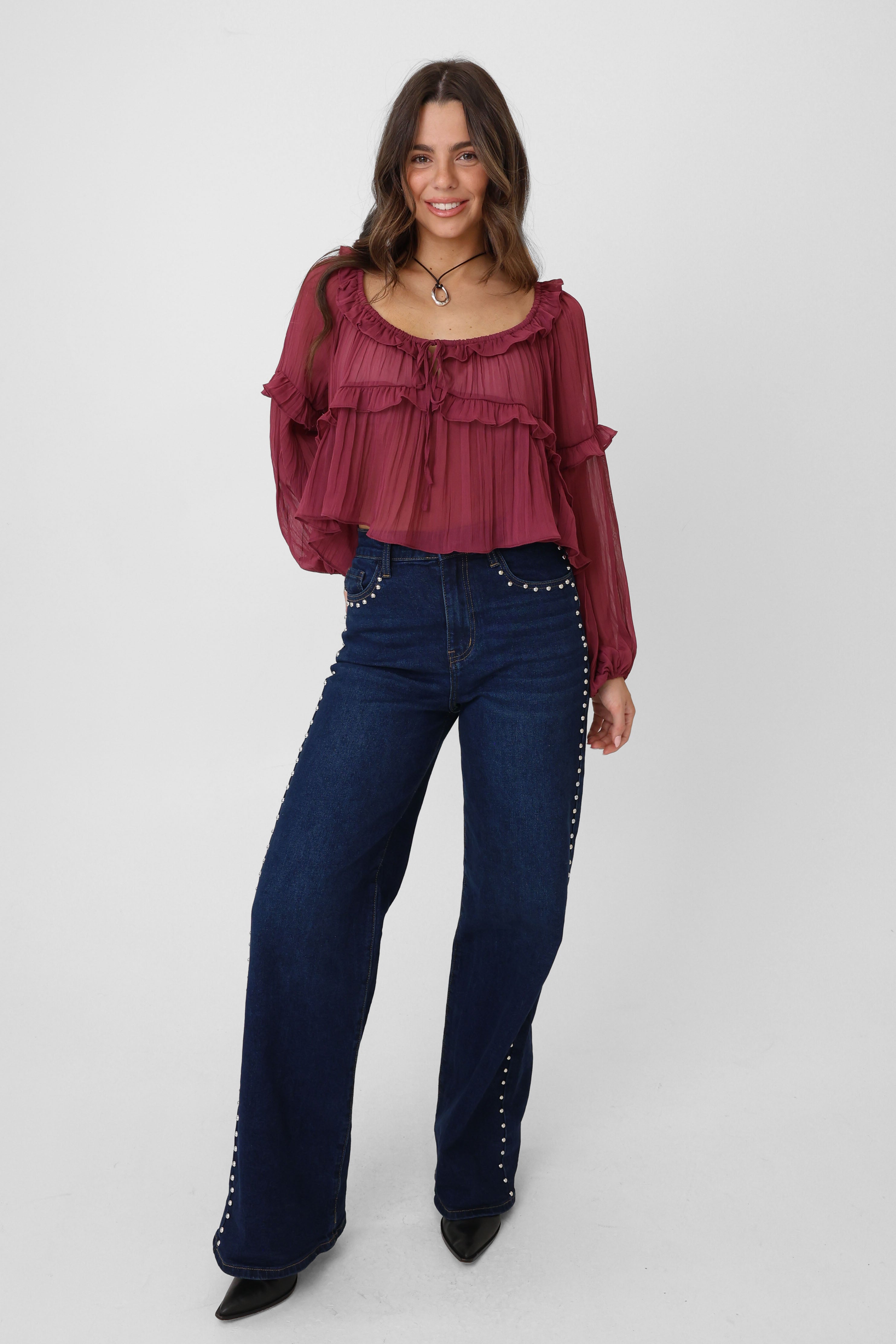 Woman wearing a burgundy top and blue jeans with studded details on a white background