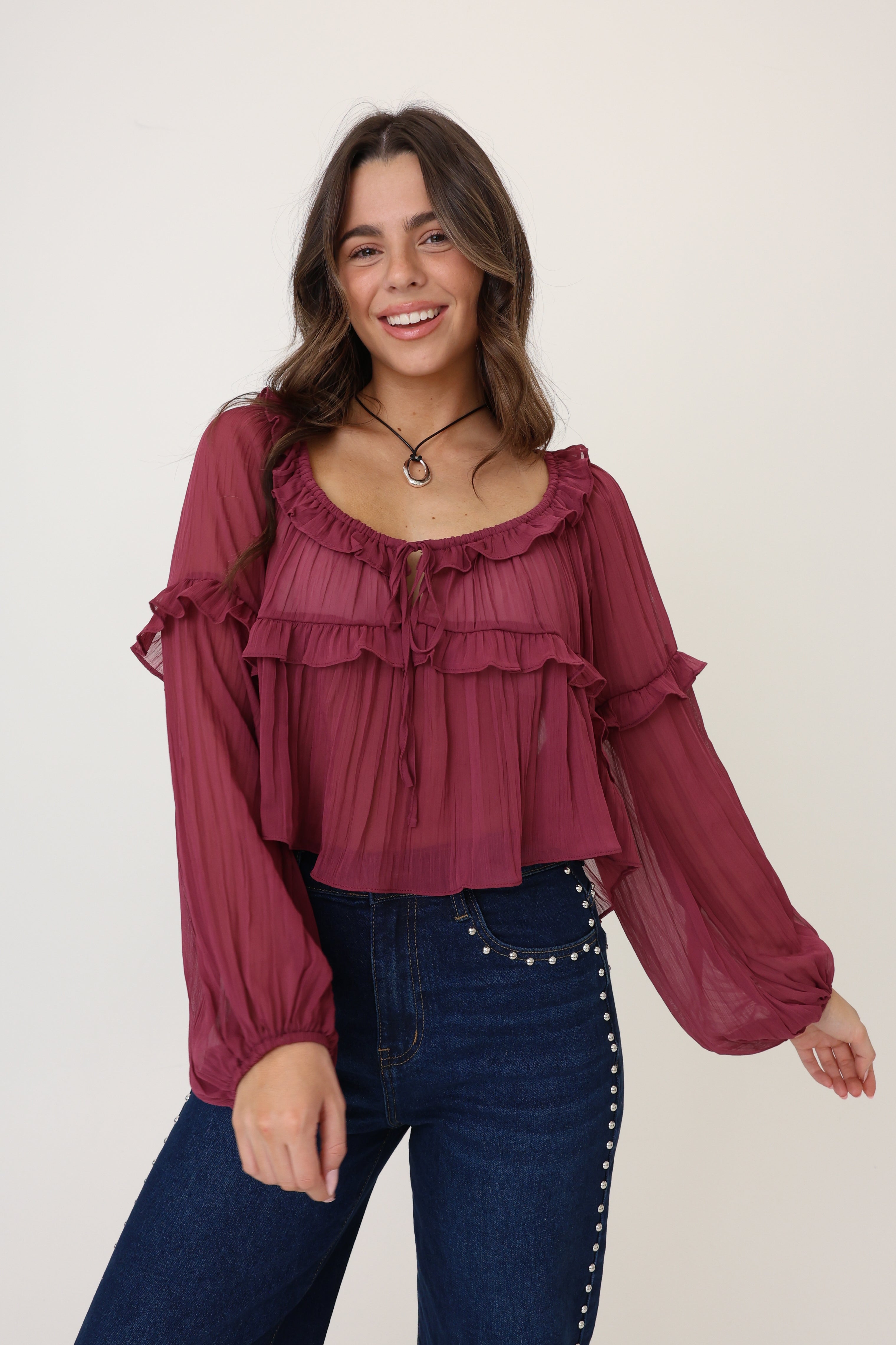 Woman wearing a burgundy ruffled blouse and blue jeans on a white background