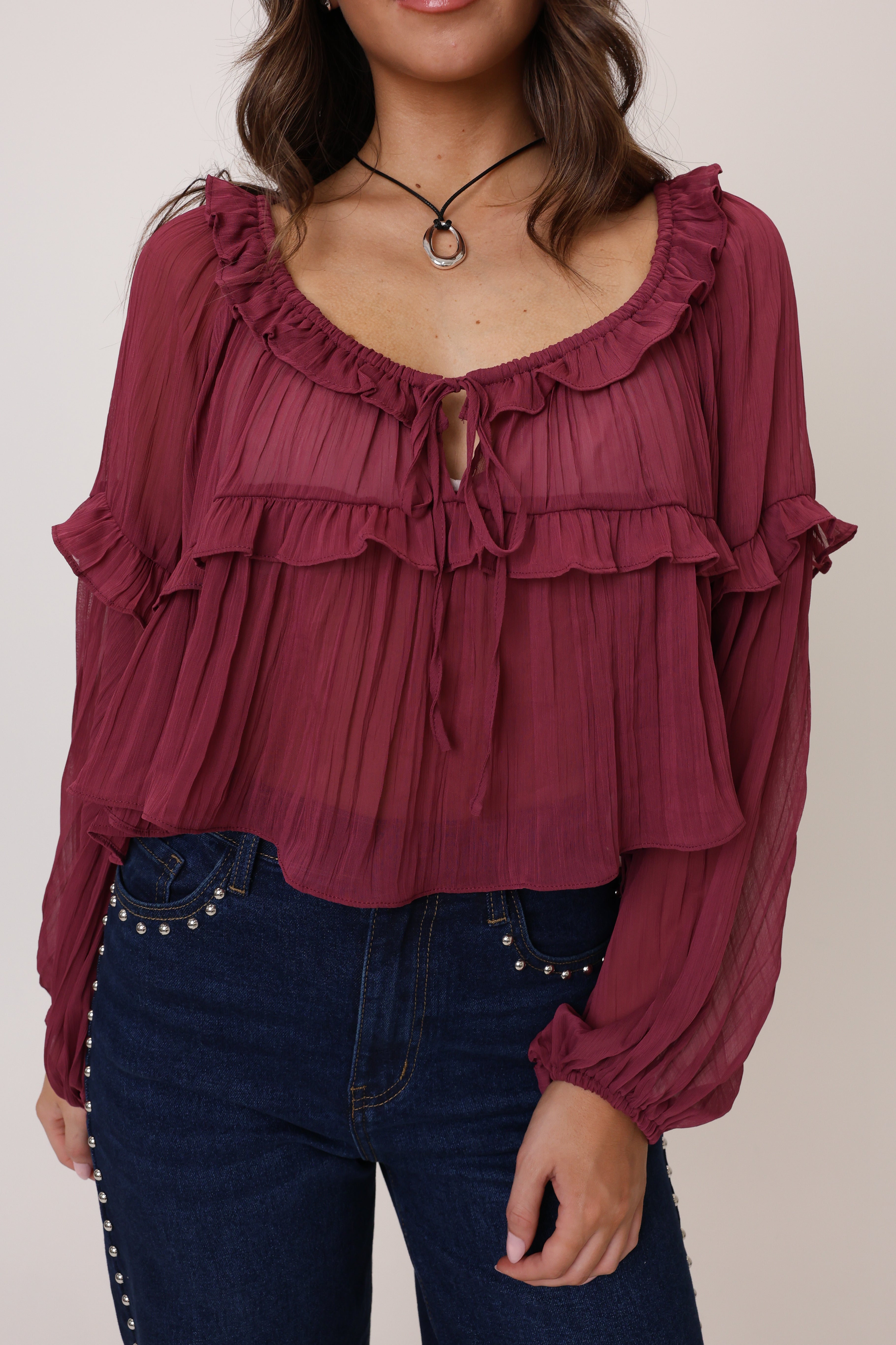 Woman wearing a burgundy ruffled blouse with long sleeves against a neutral background