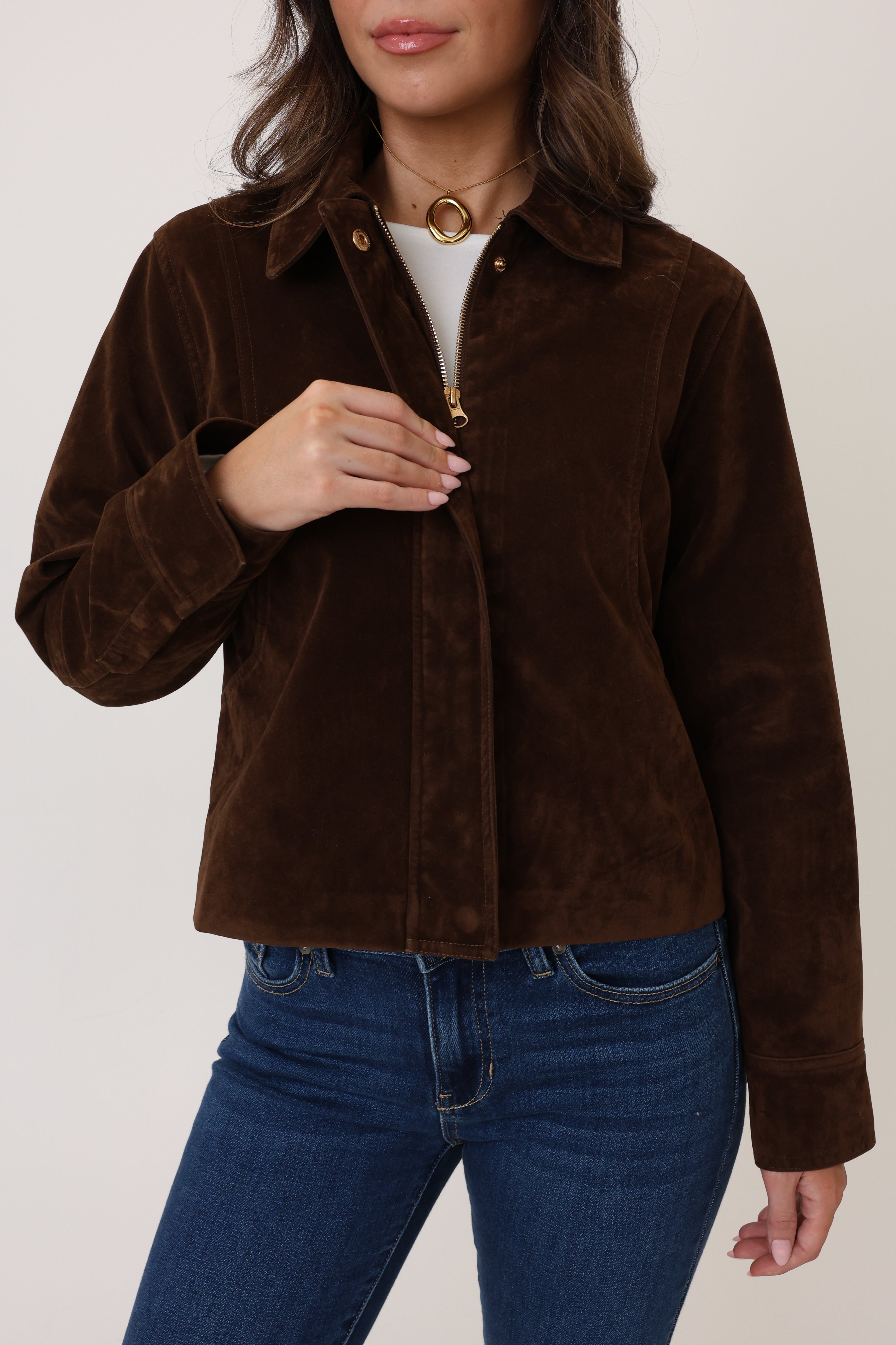 Person wearing a brown corduroy jacket and blue jeans on a plain background