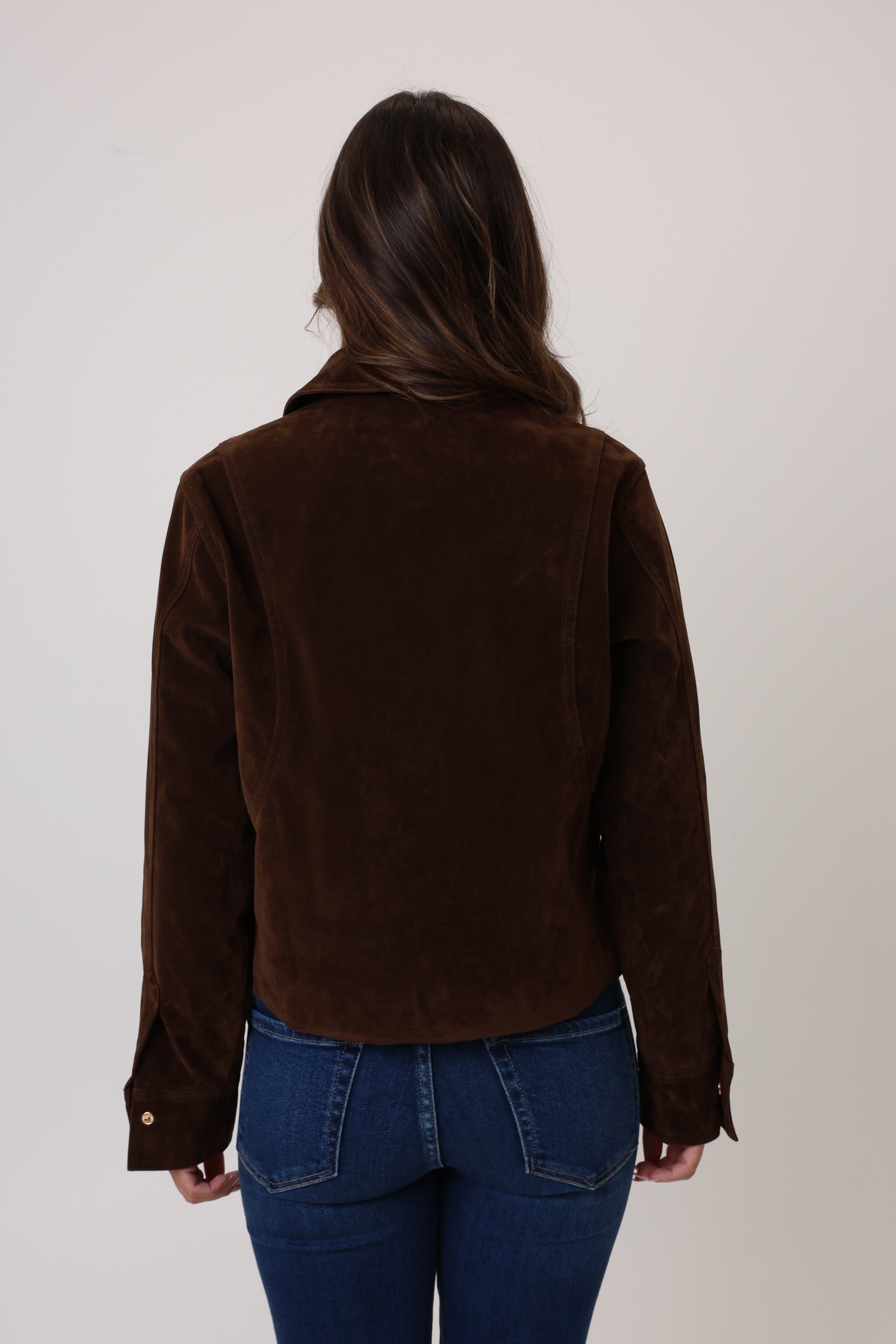 Person wearing a brown jacket and blue jeans on a plain background