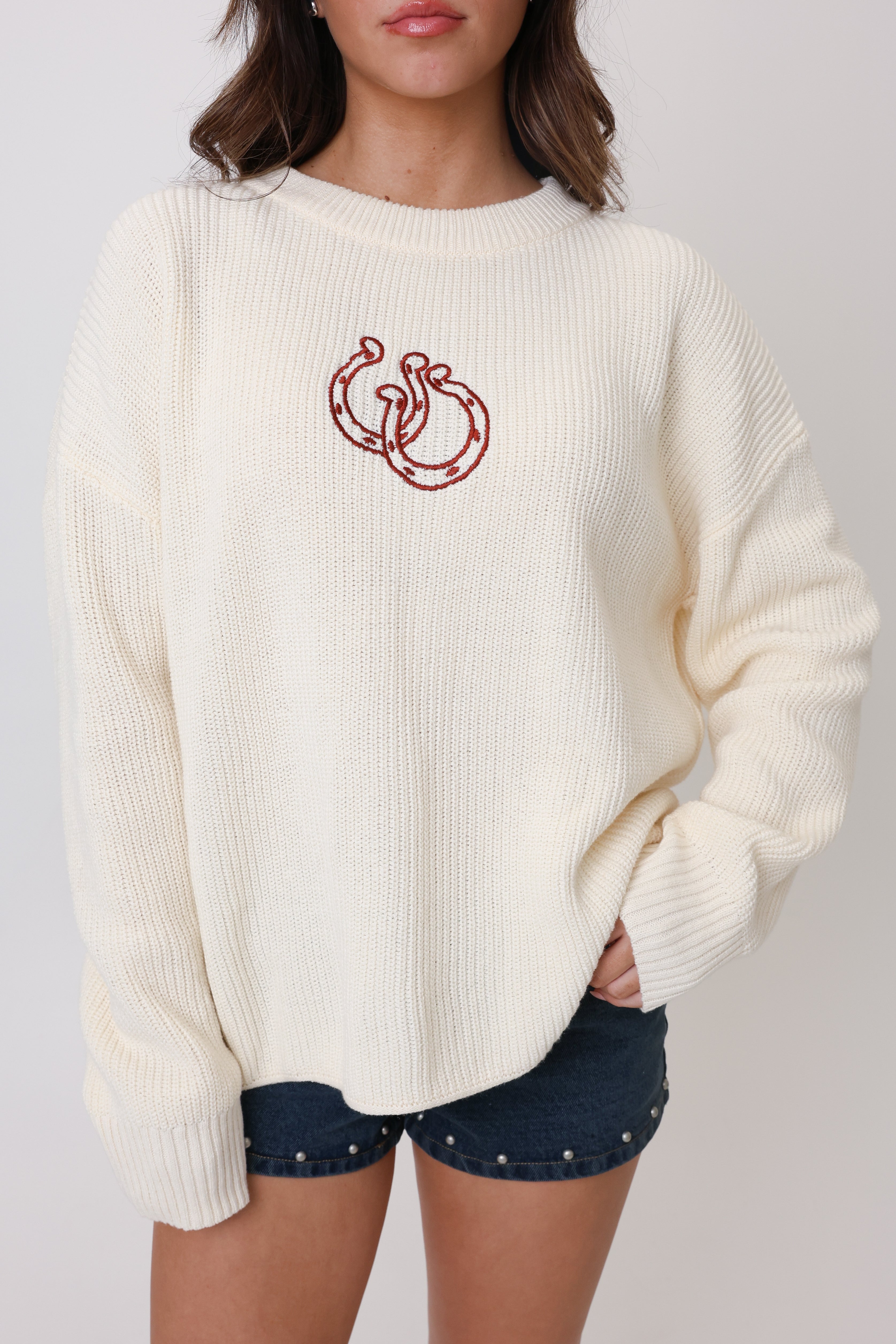 White sweater with red logo worn by a person on a plain background