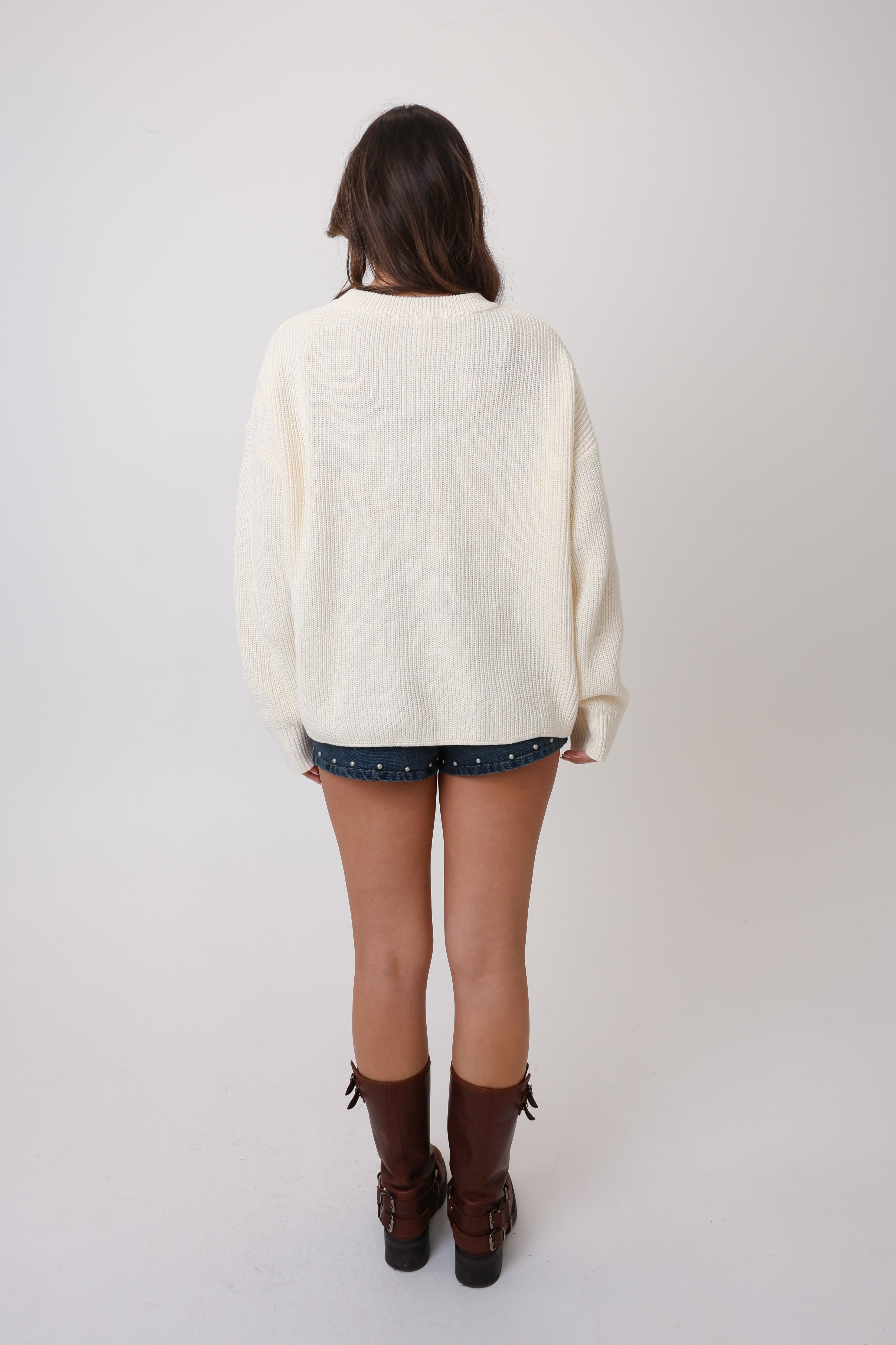 Person wearing a cream sweater and brown boots on a white background