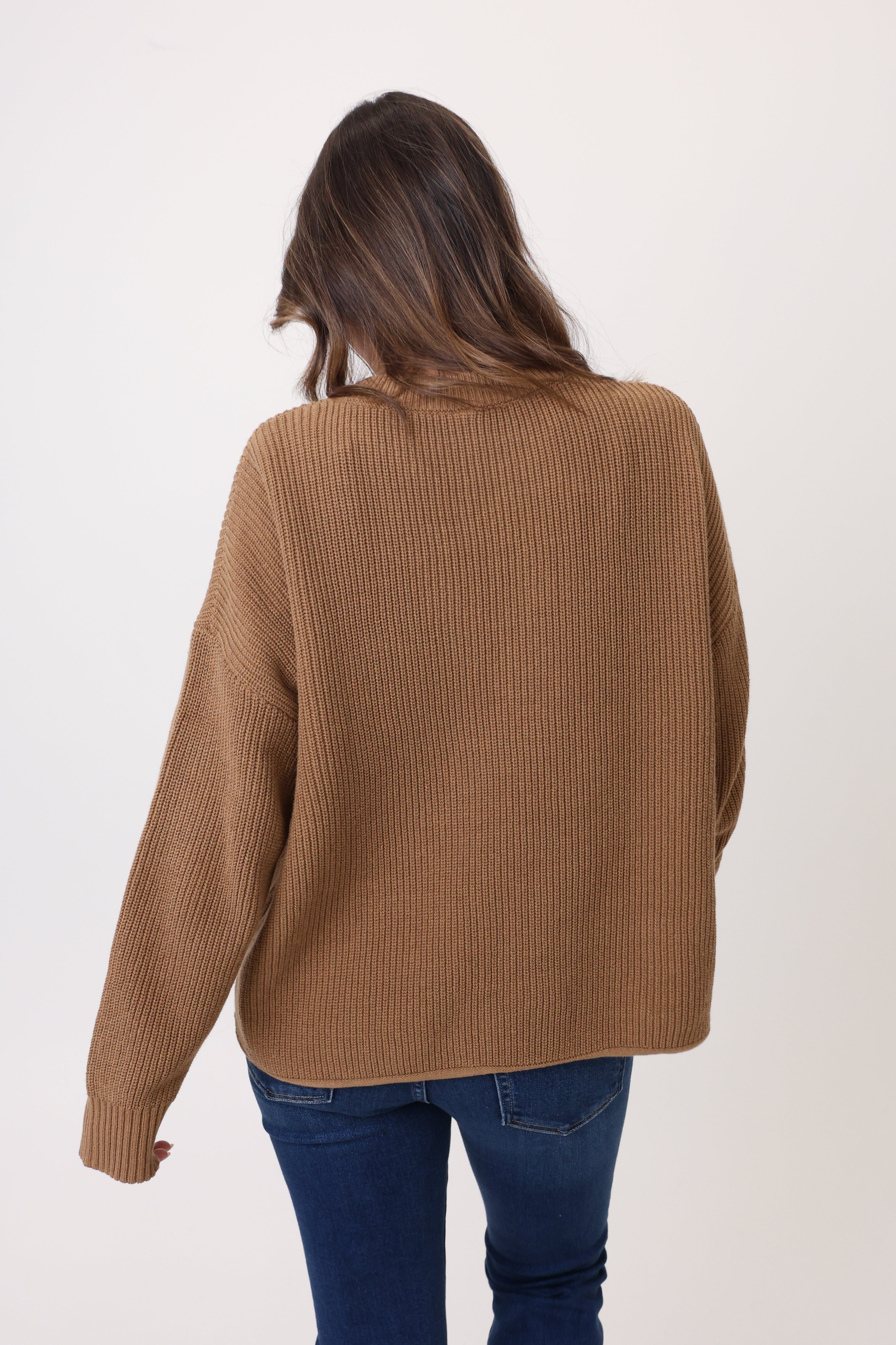 Person wearing a brown ribbed sweater and blue jeans on a white background