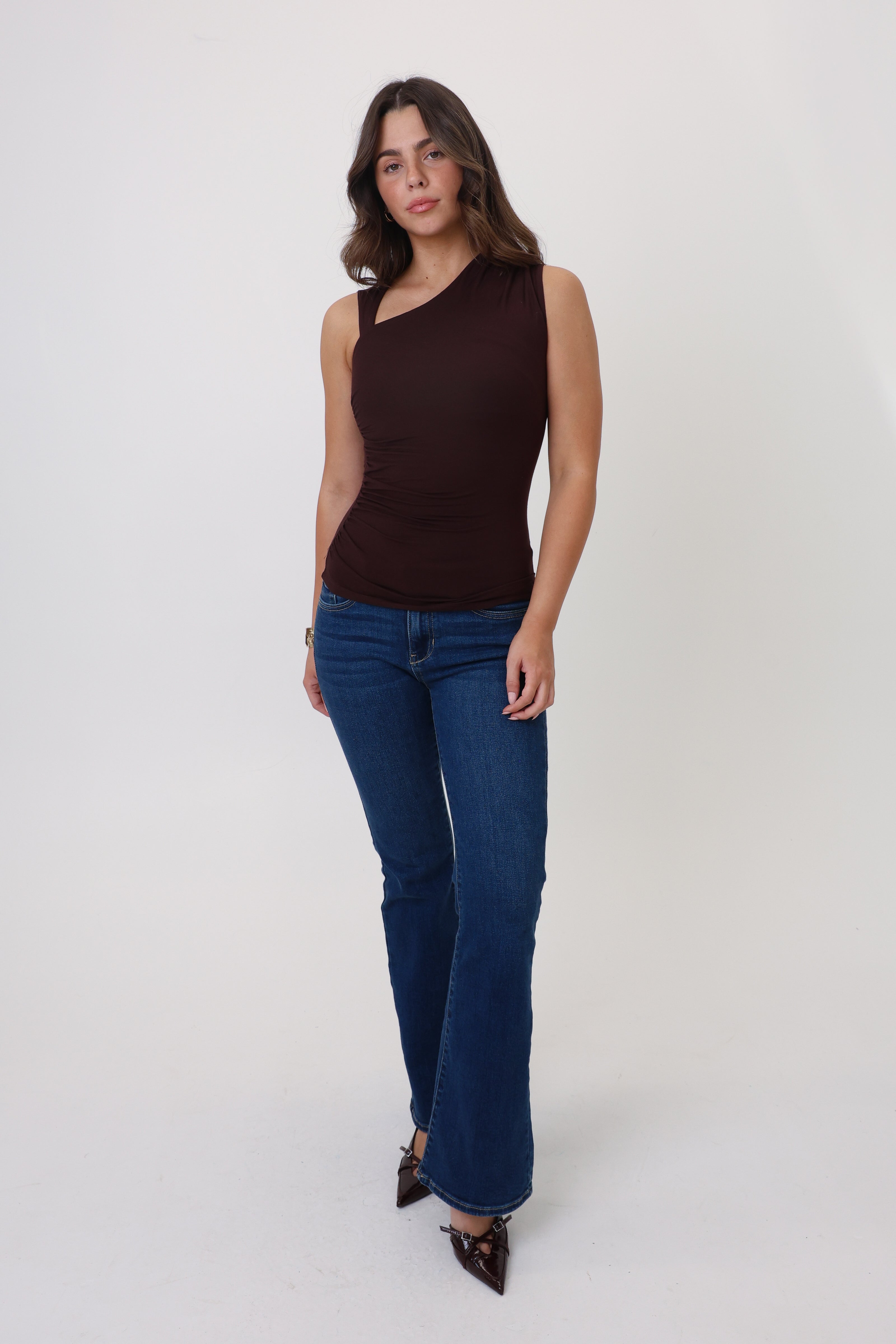 Woman wearing a brown one-shoulder top and blue jeans on a white background