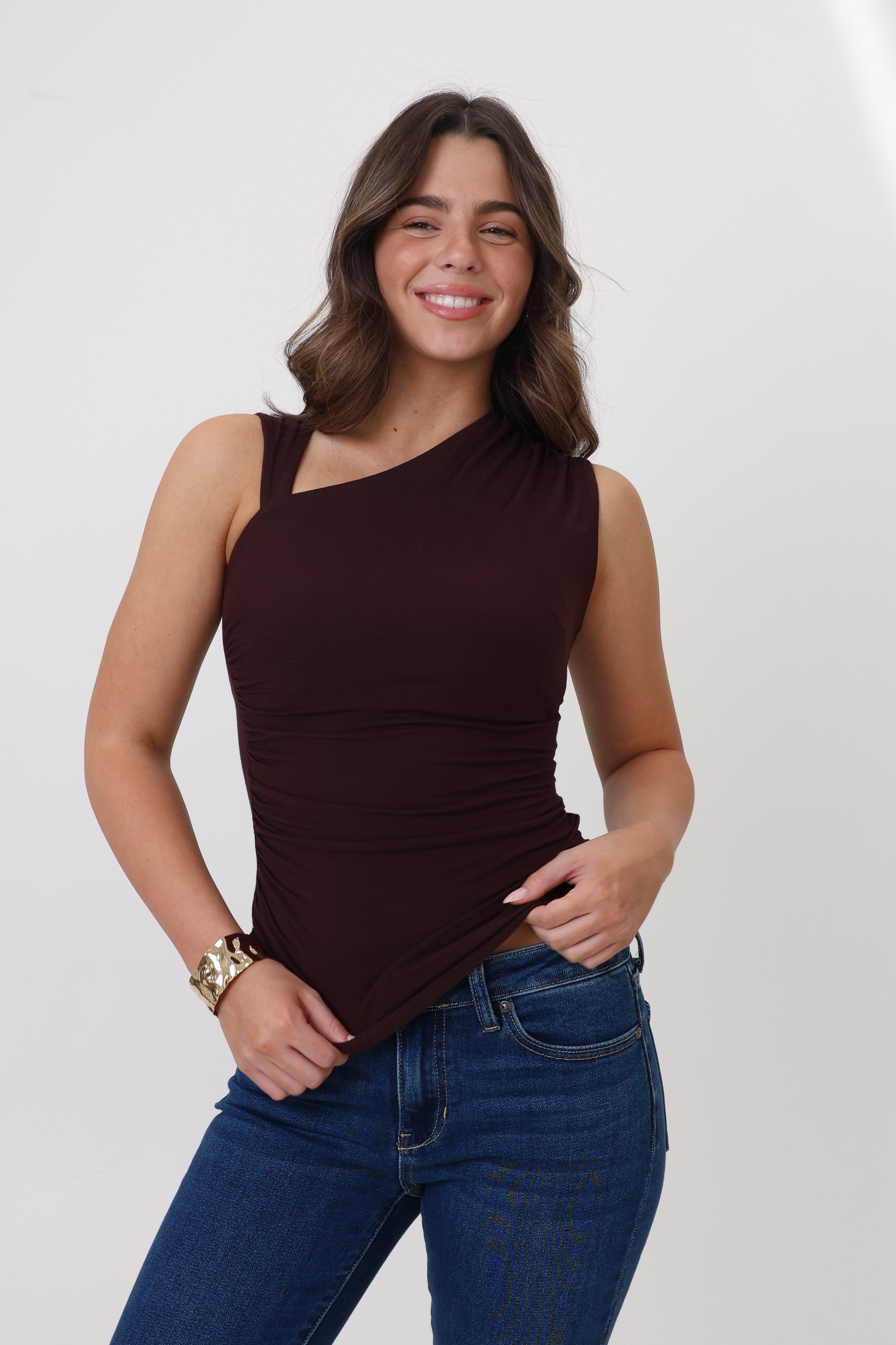 Woman wearing a brown one-shoulder top and blue jeans against a white background