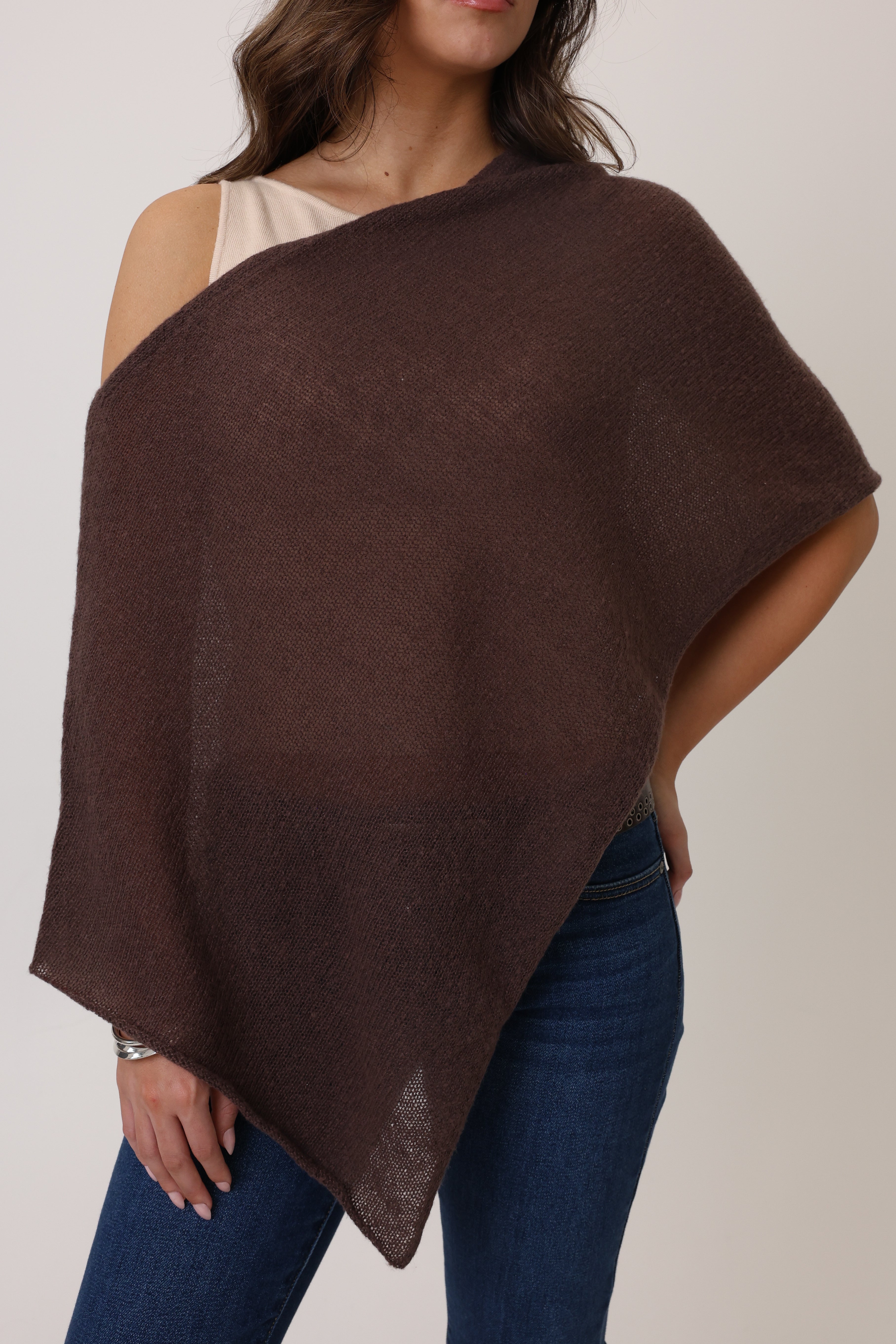 Woman wearing a brown poncho over one shoulder against a plain background