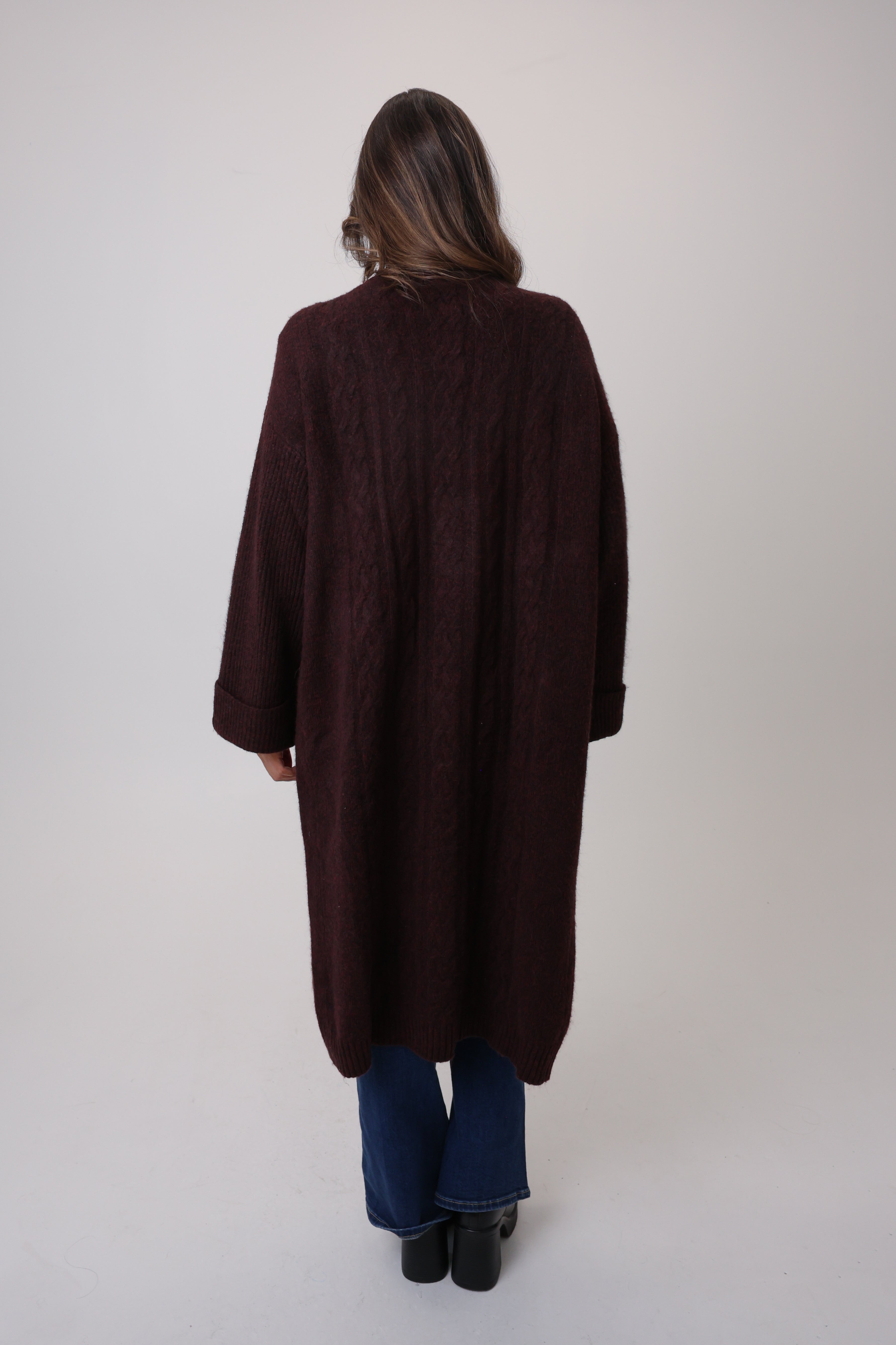 Person wearing a long brown coat on a plain background