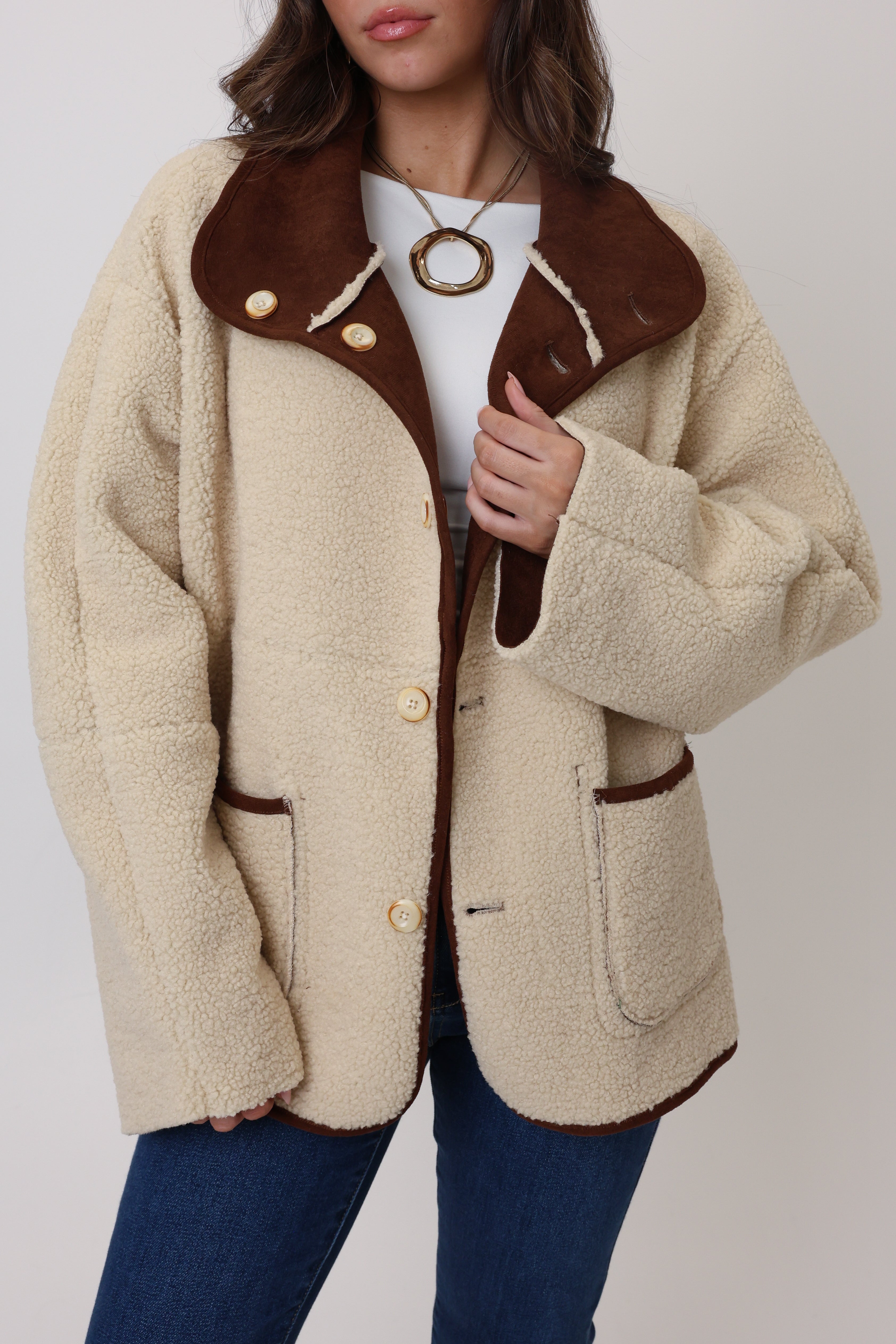 Beige coat with brown leather accents worn by a person on a plain background