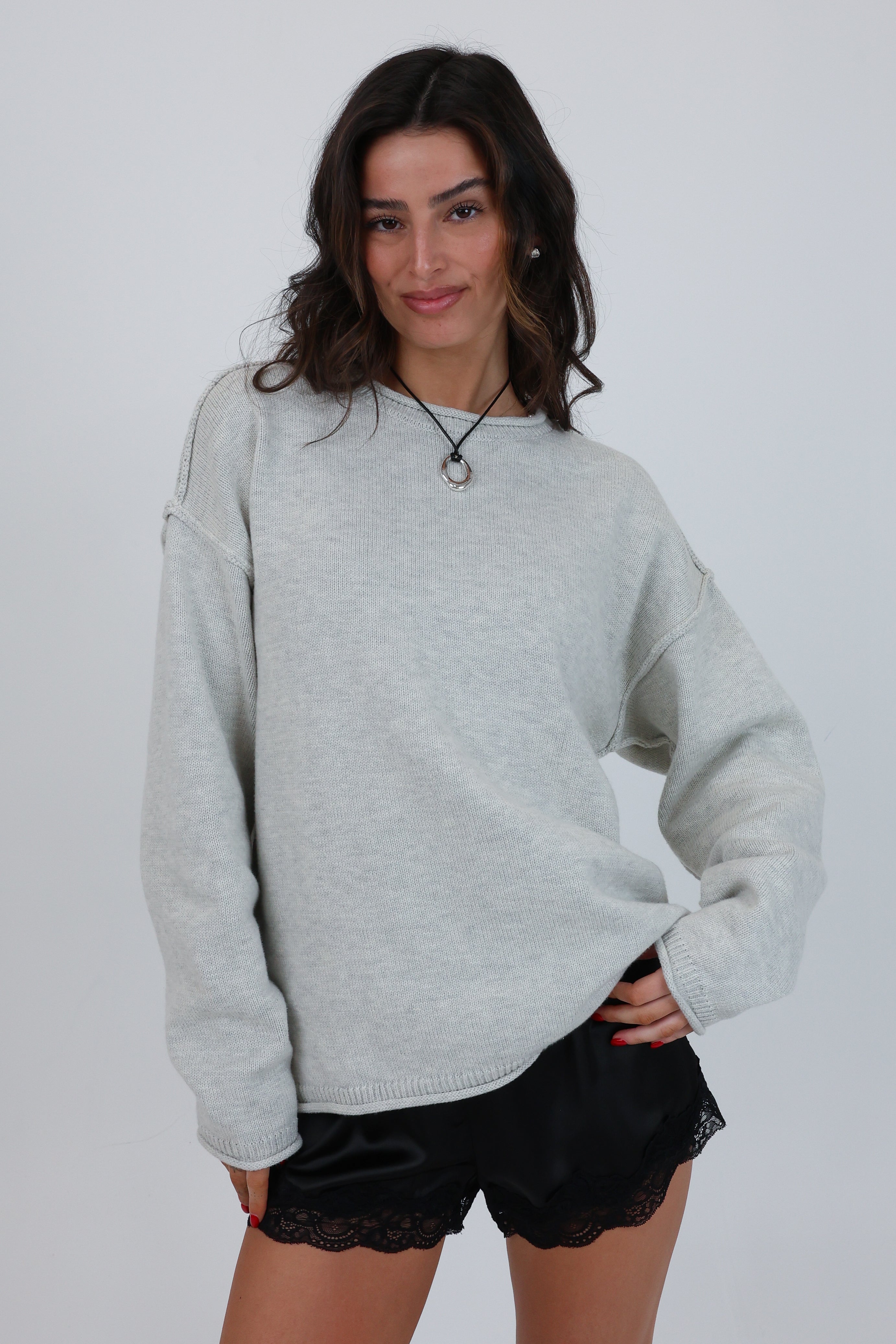 Woman wearing a light gray sweater and black shorts on a plain background