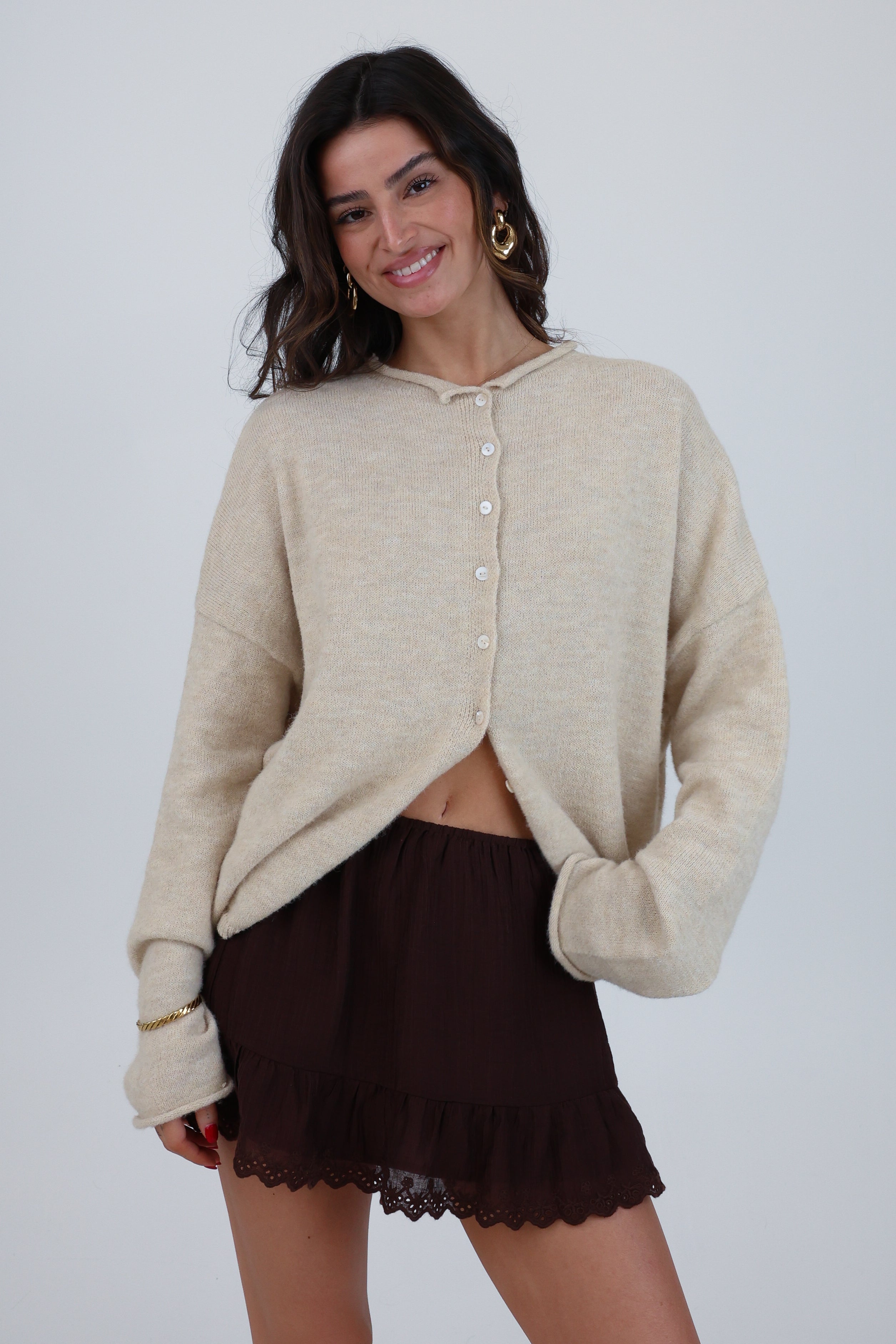 Woman wearing a beige cardigan over a brown skirt on a plain background