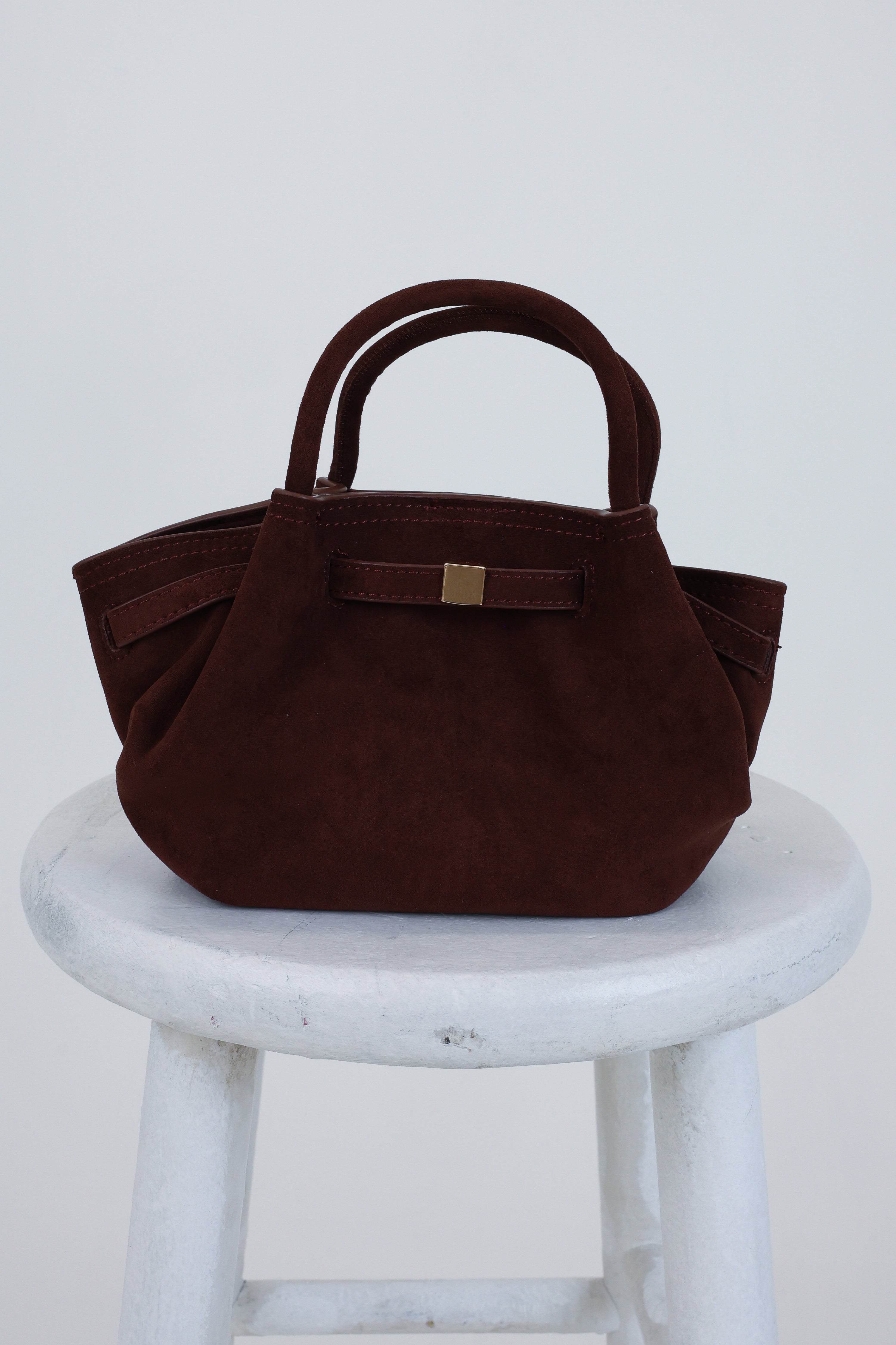 Brown handbag on a white stool against a light gray background