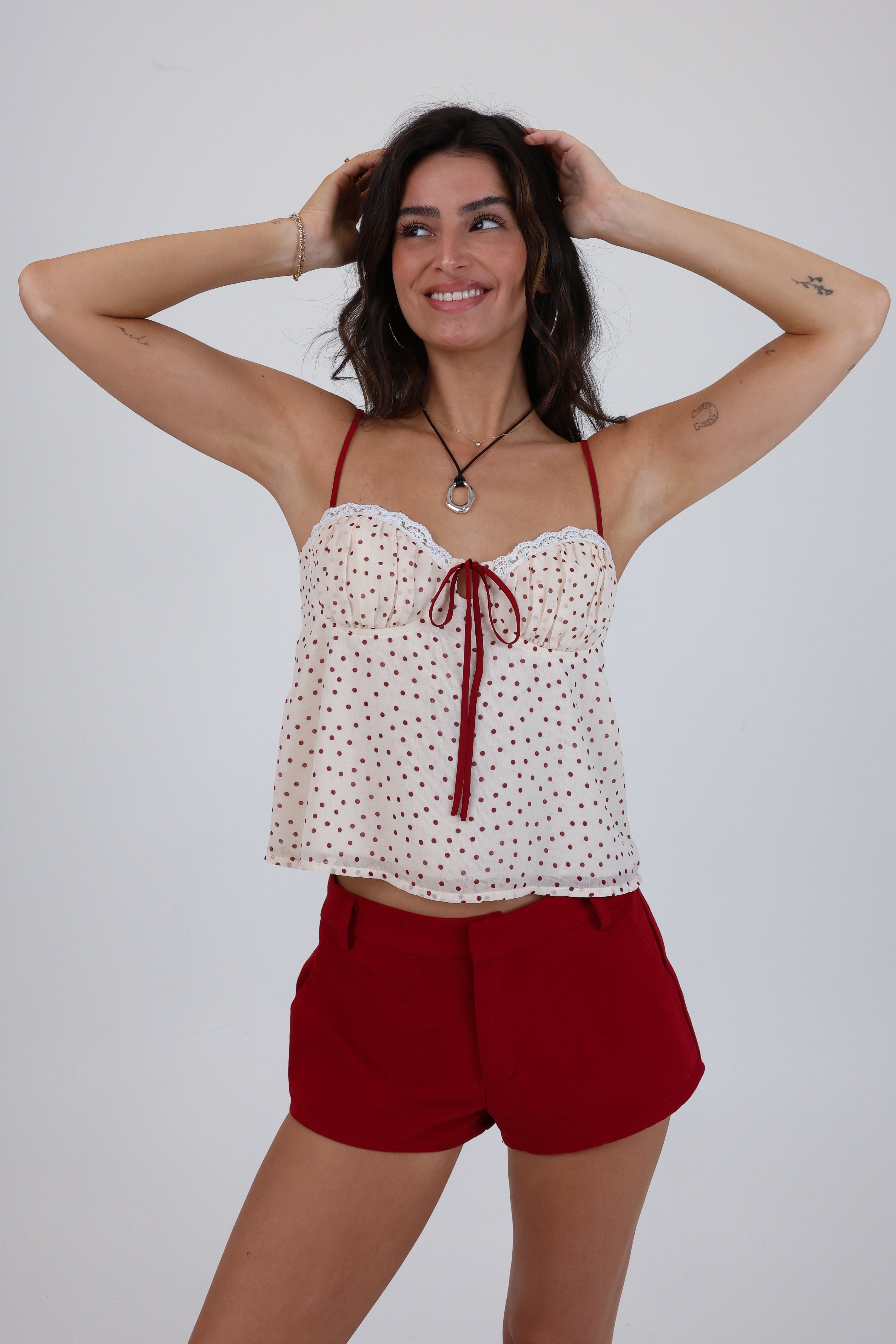 Woman wearing a white top with red straps and red shorts on a plain background