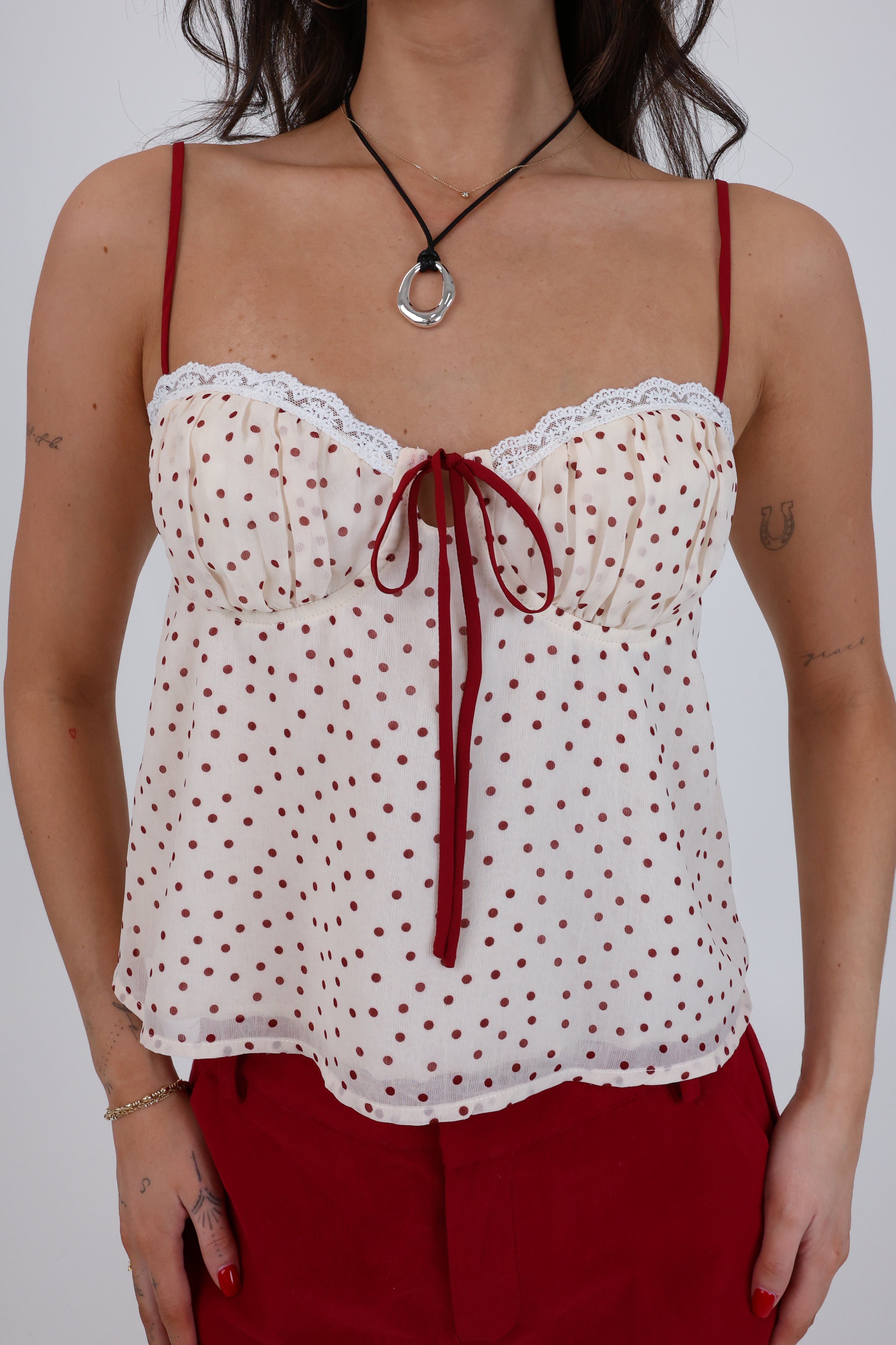 Woman wearing a white polka dot top with red straps and red pants against a plain background