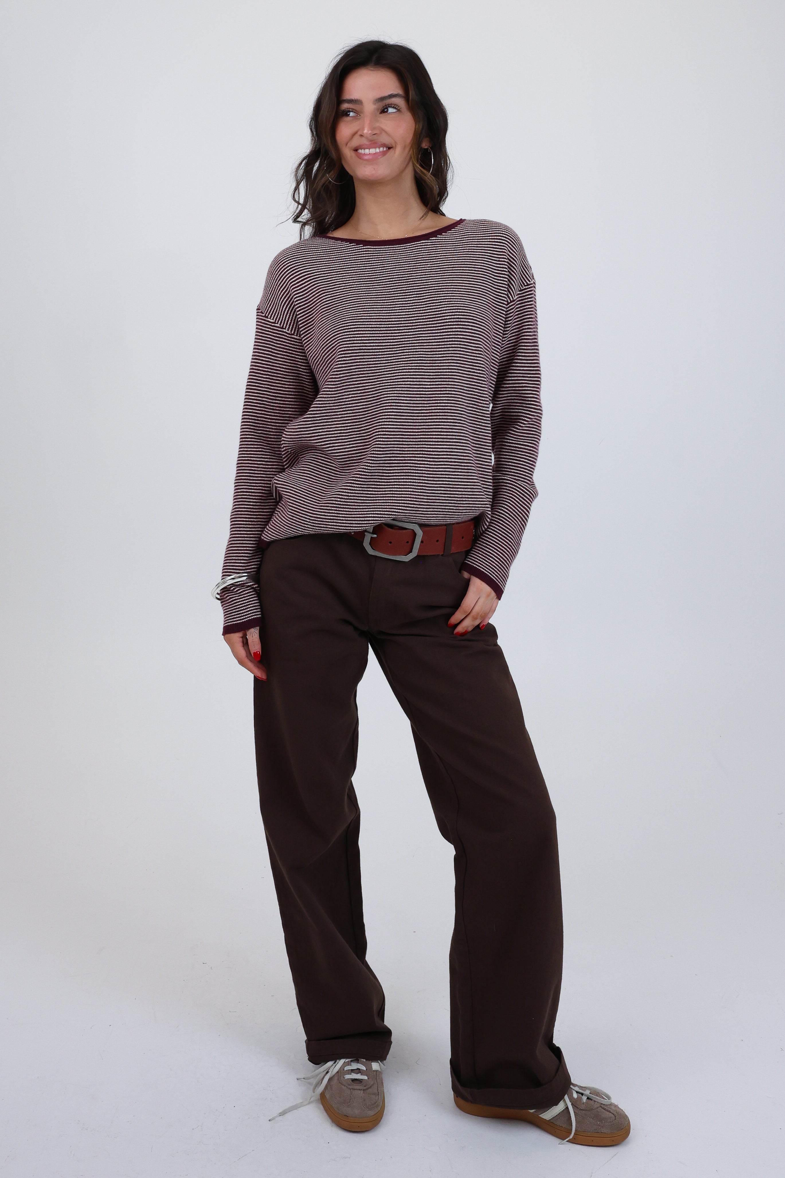 Woman wearing a brown sweater and dark pants on a white background