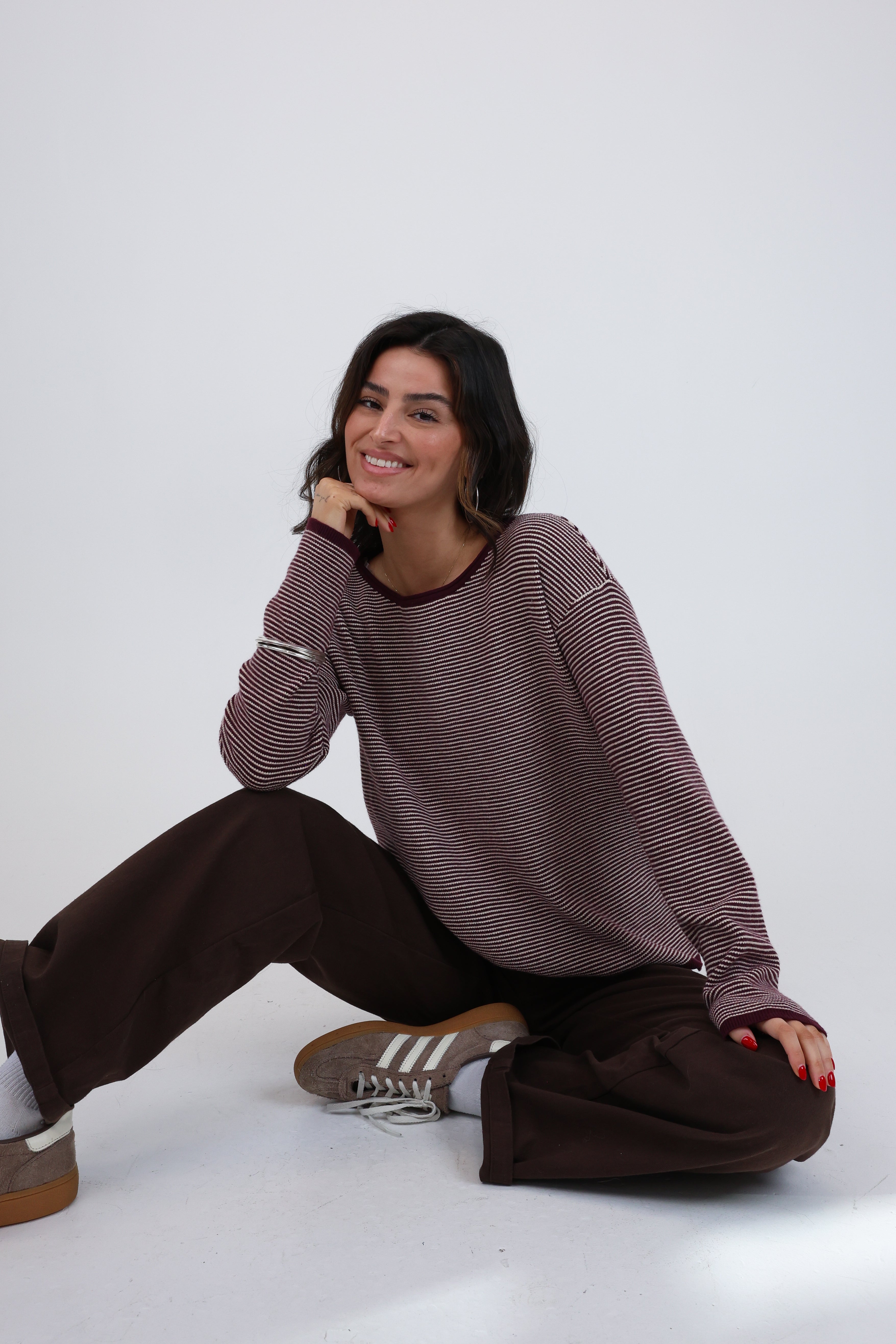 Woman sitting on a white floor wearing a brown sweater and dark pants.