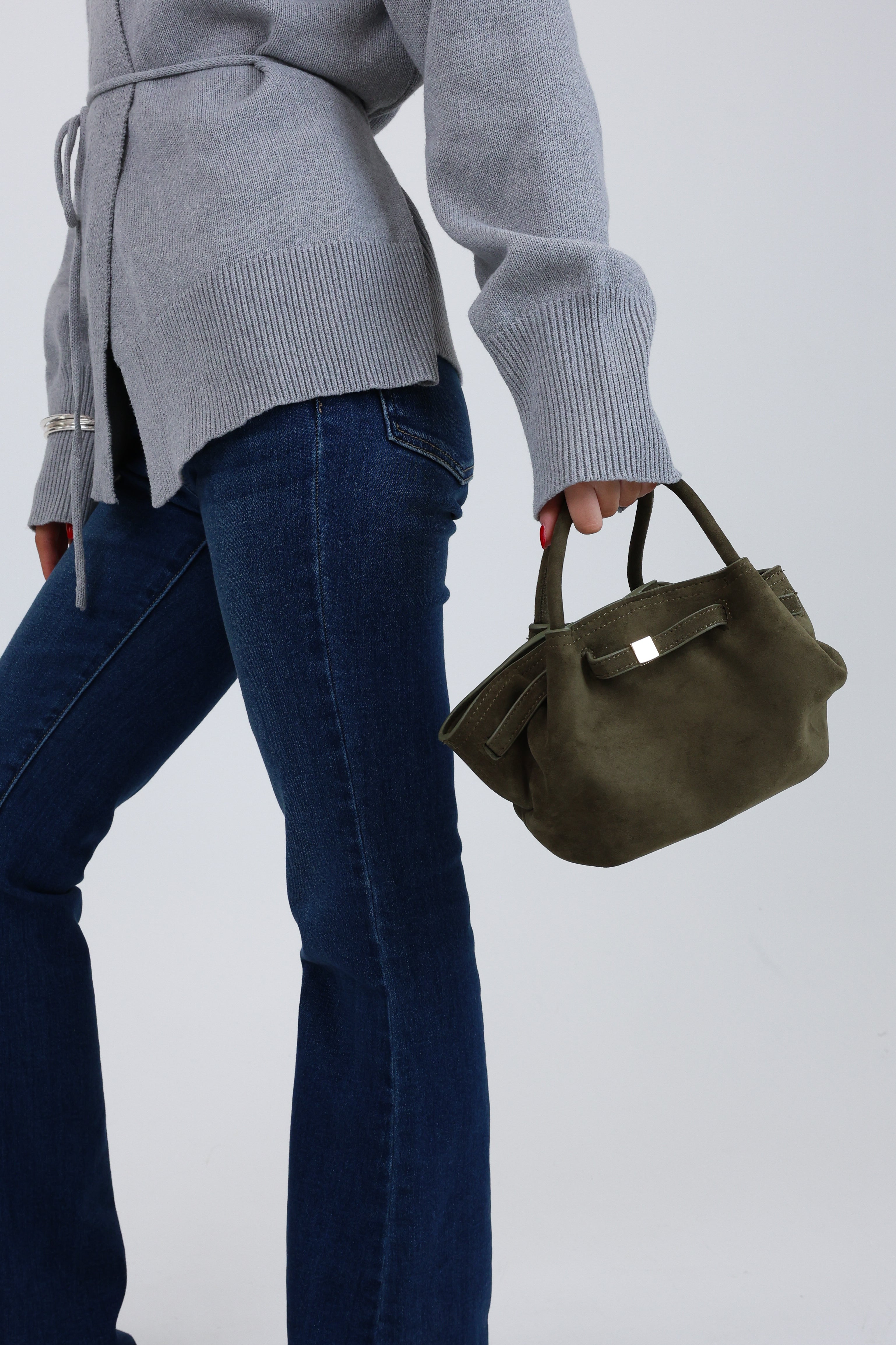 Person wearing a gray sweater and blue jeans holding a green handbag on a white background