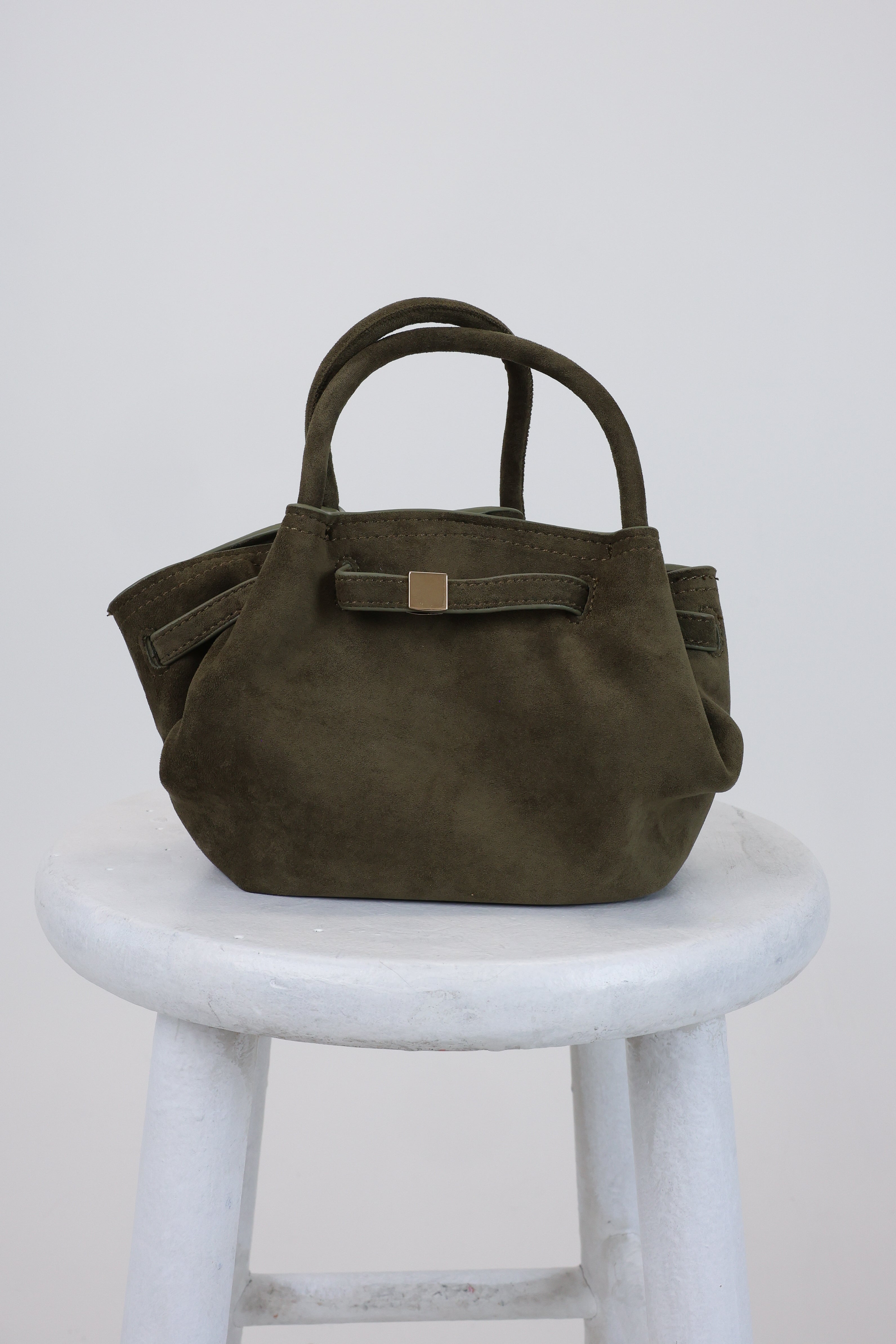 Green handbag on a white stool against a light gray background