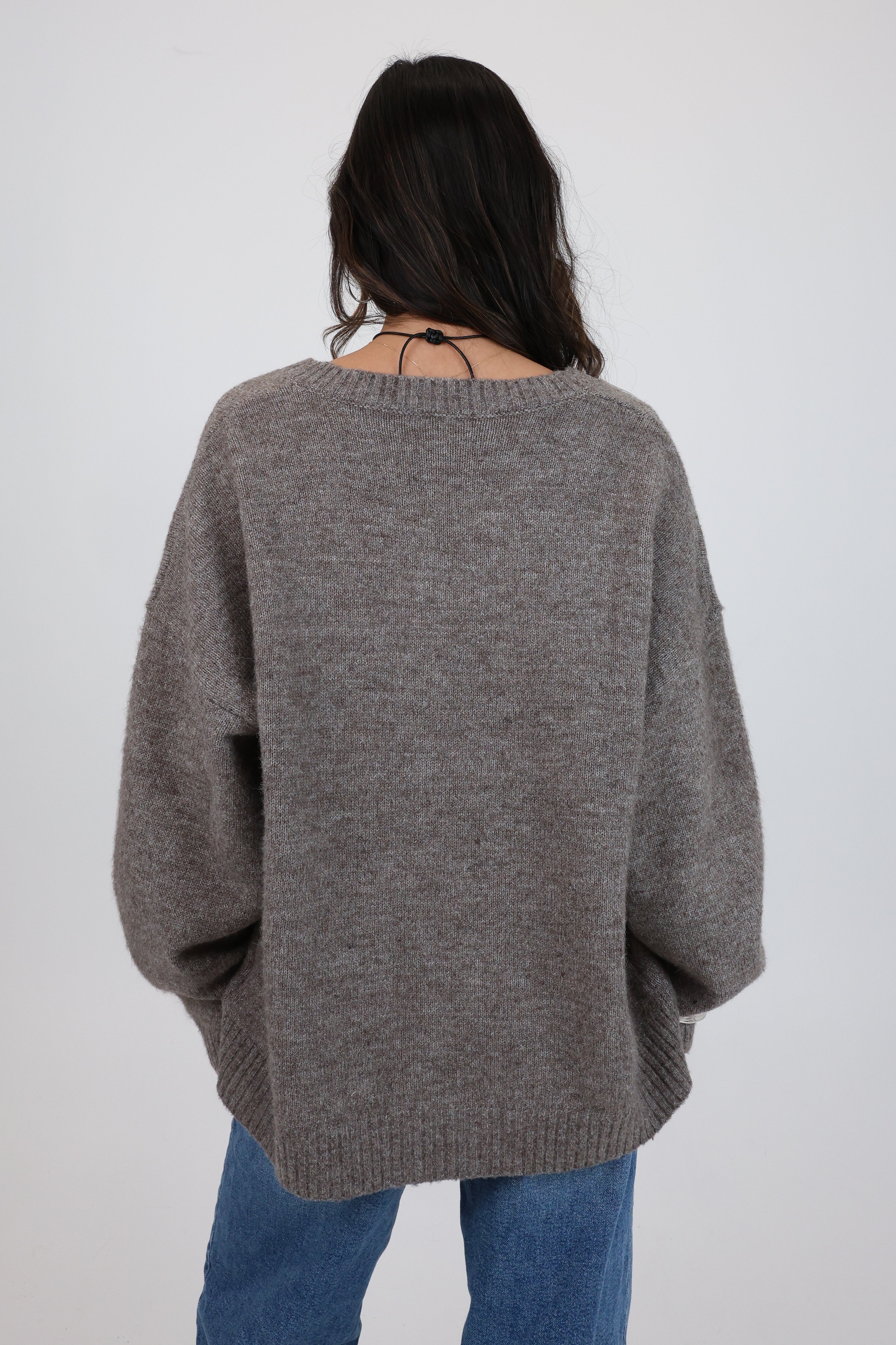 Person wearing a gray sweater and blue jeans on a white background