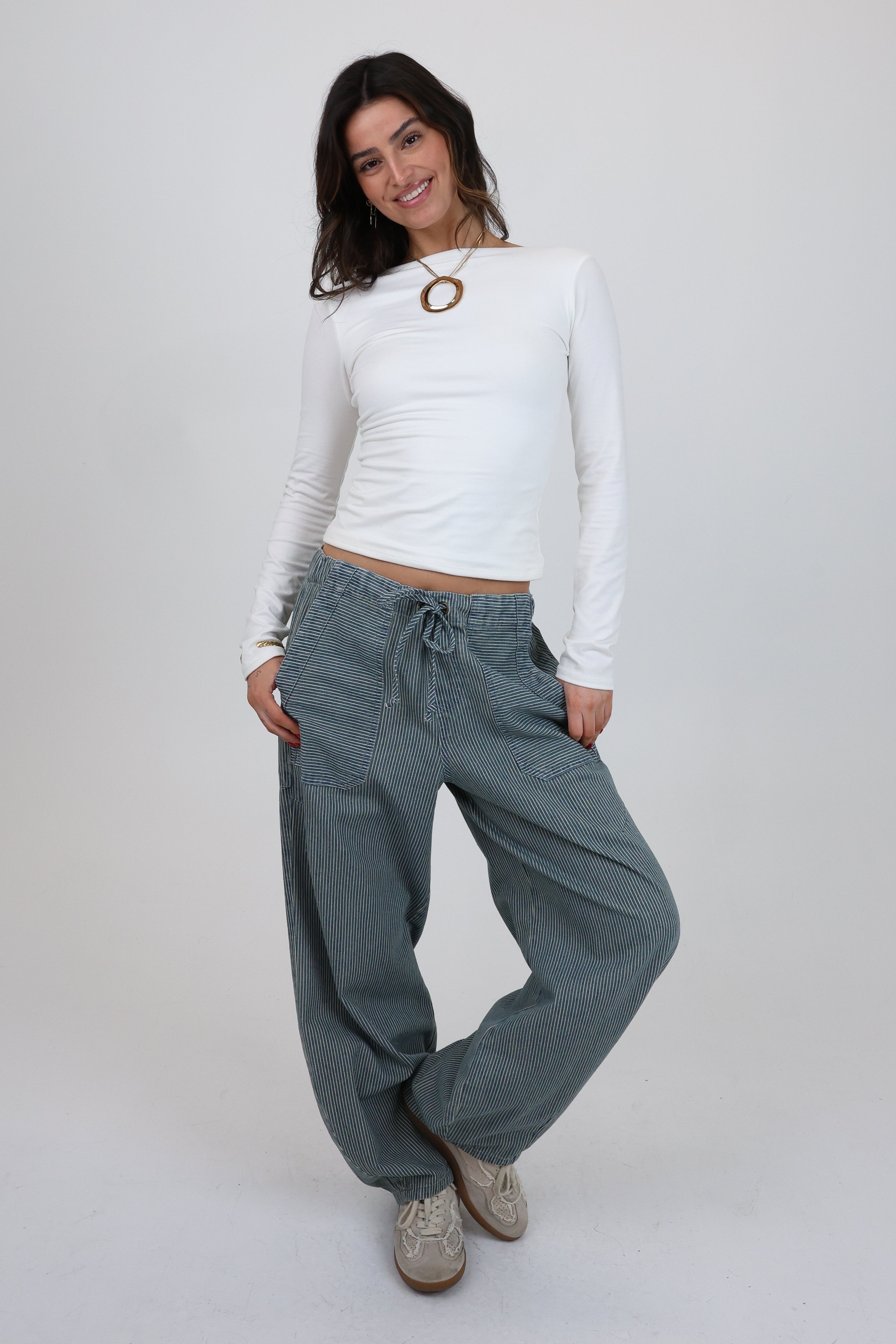 Woman wearing a white long-sleeve top and blue pants on a plain background