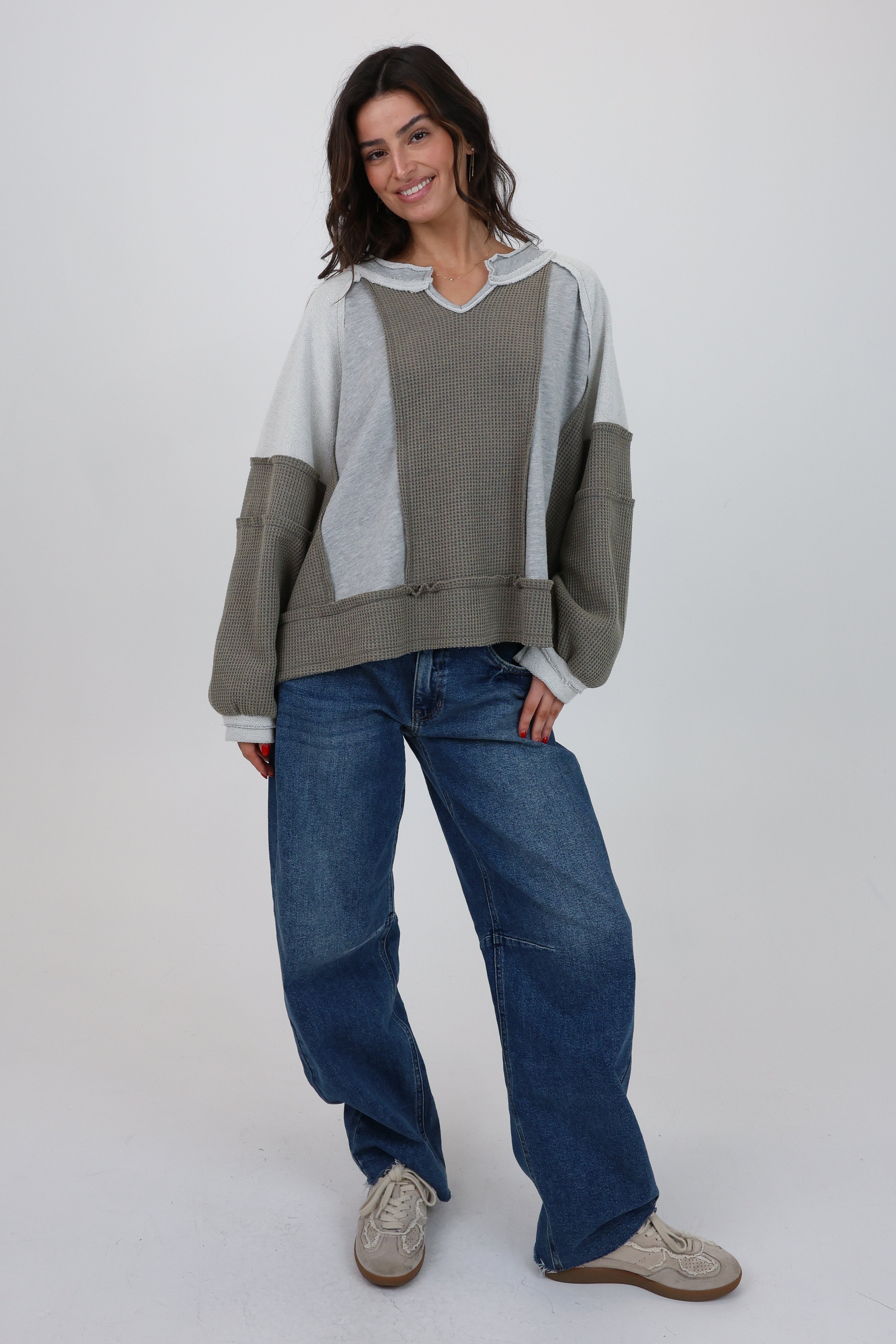 Woman wearing a color-blocked sweater and blue jeans on a white background