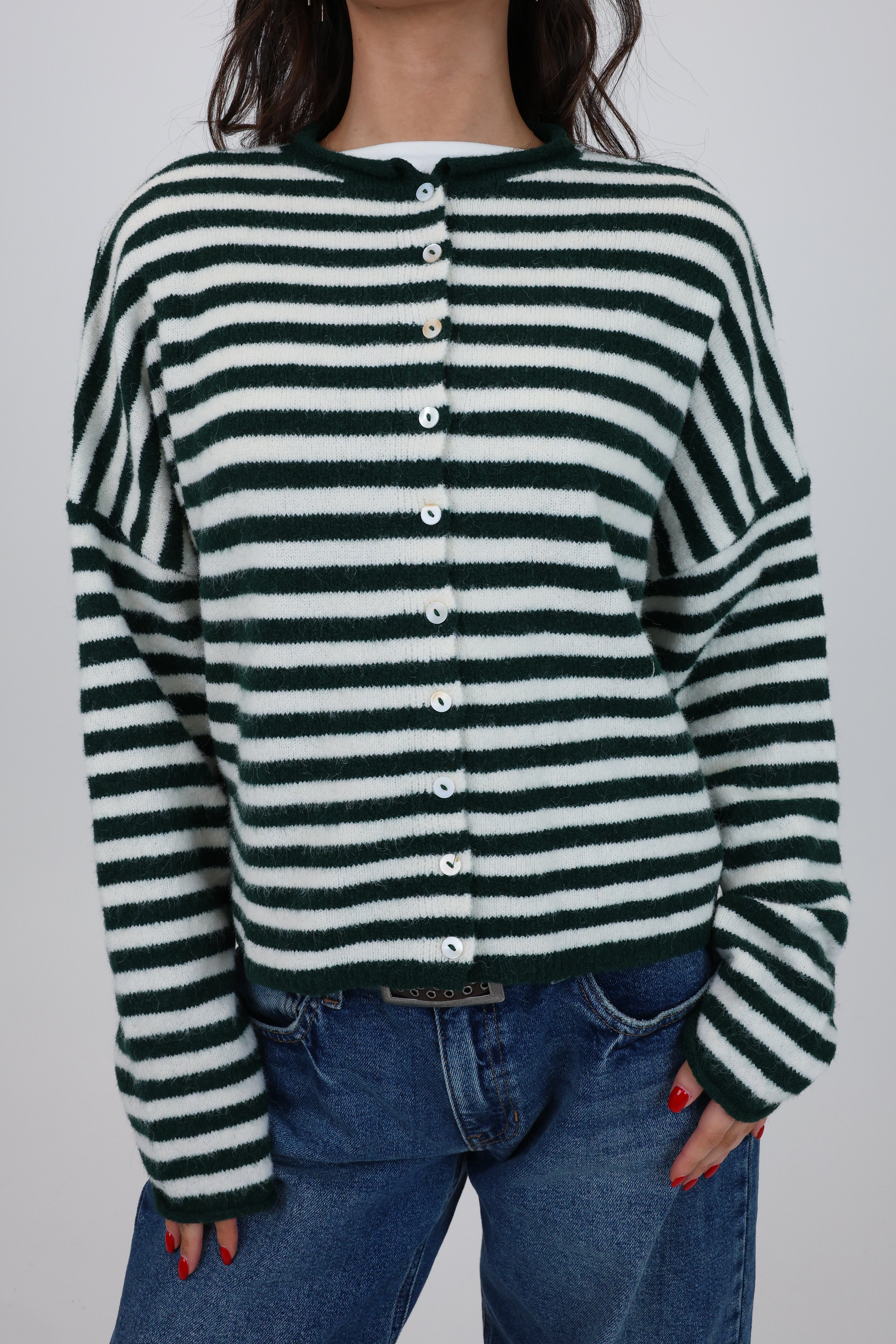 Person wearing a green and white striped sweater with blue jeans on a plain background