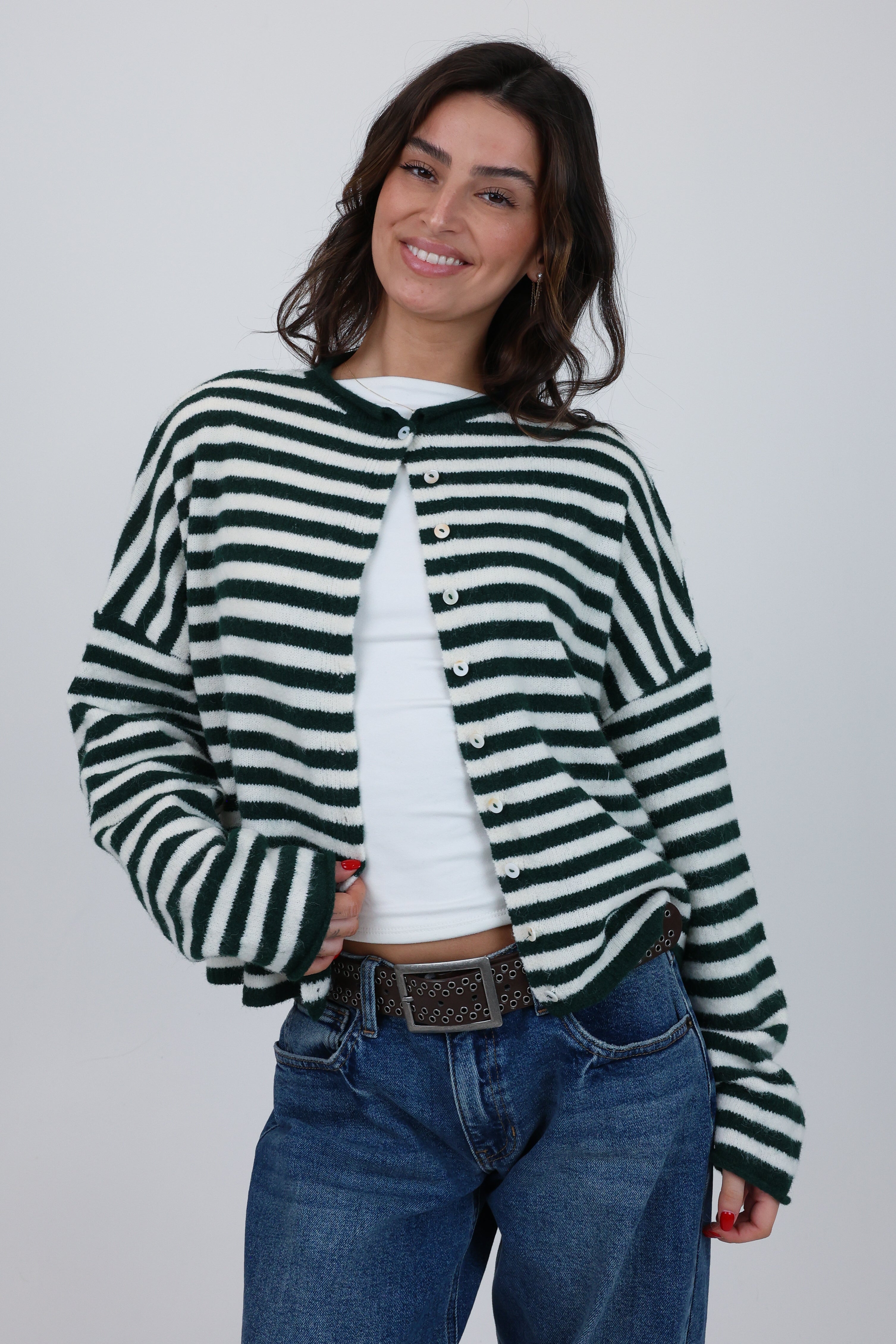 Woman wearing a green and white striped cardigan over a white shirt, standing against a plain background.