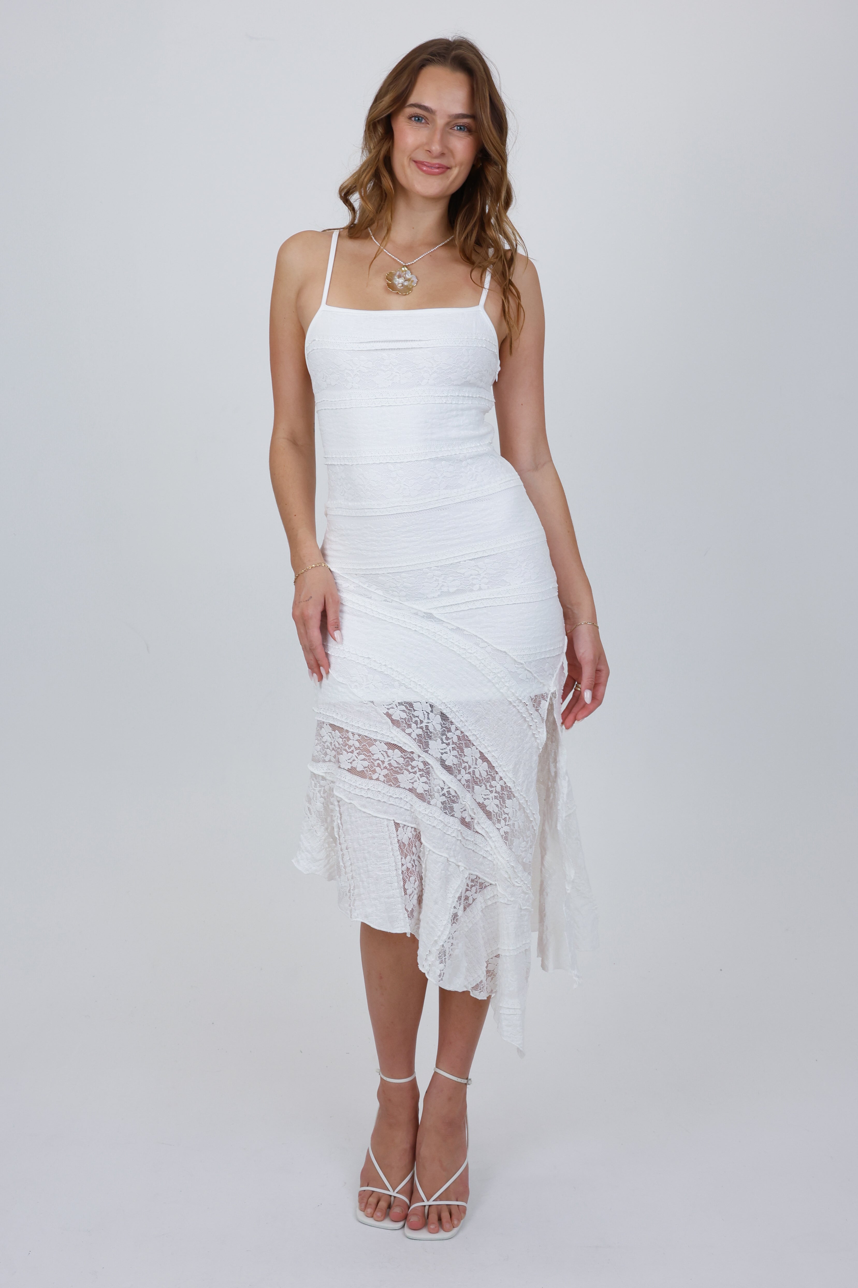 Woman wearing a white dress with lace details on a plain background