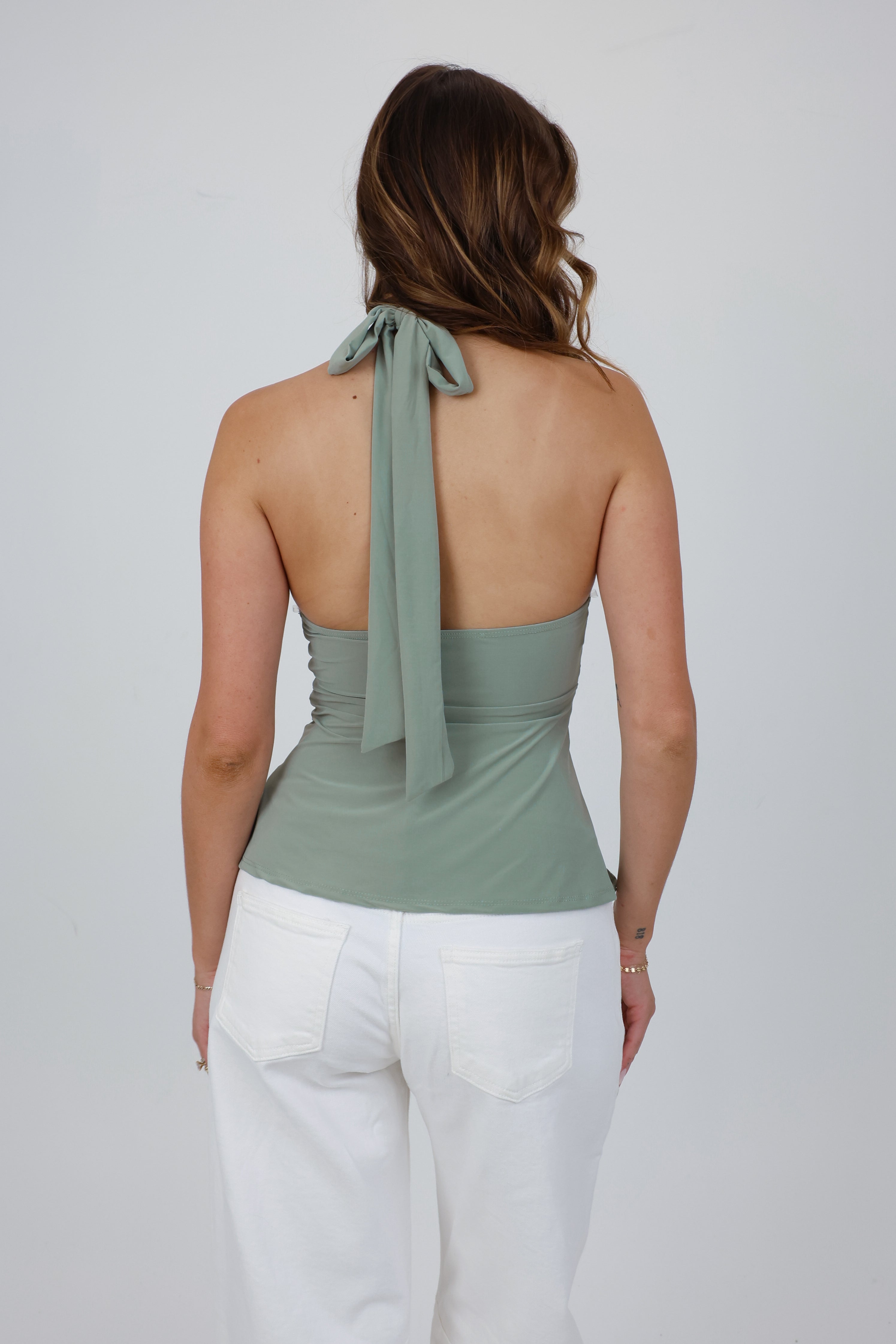 Woman wearing a green halter top with a tie detail on a white background