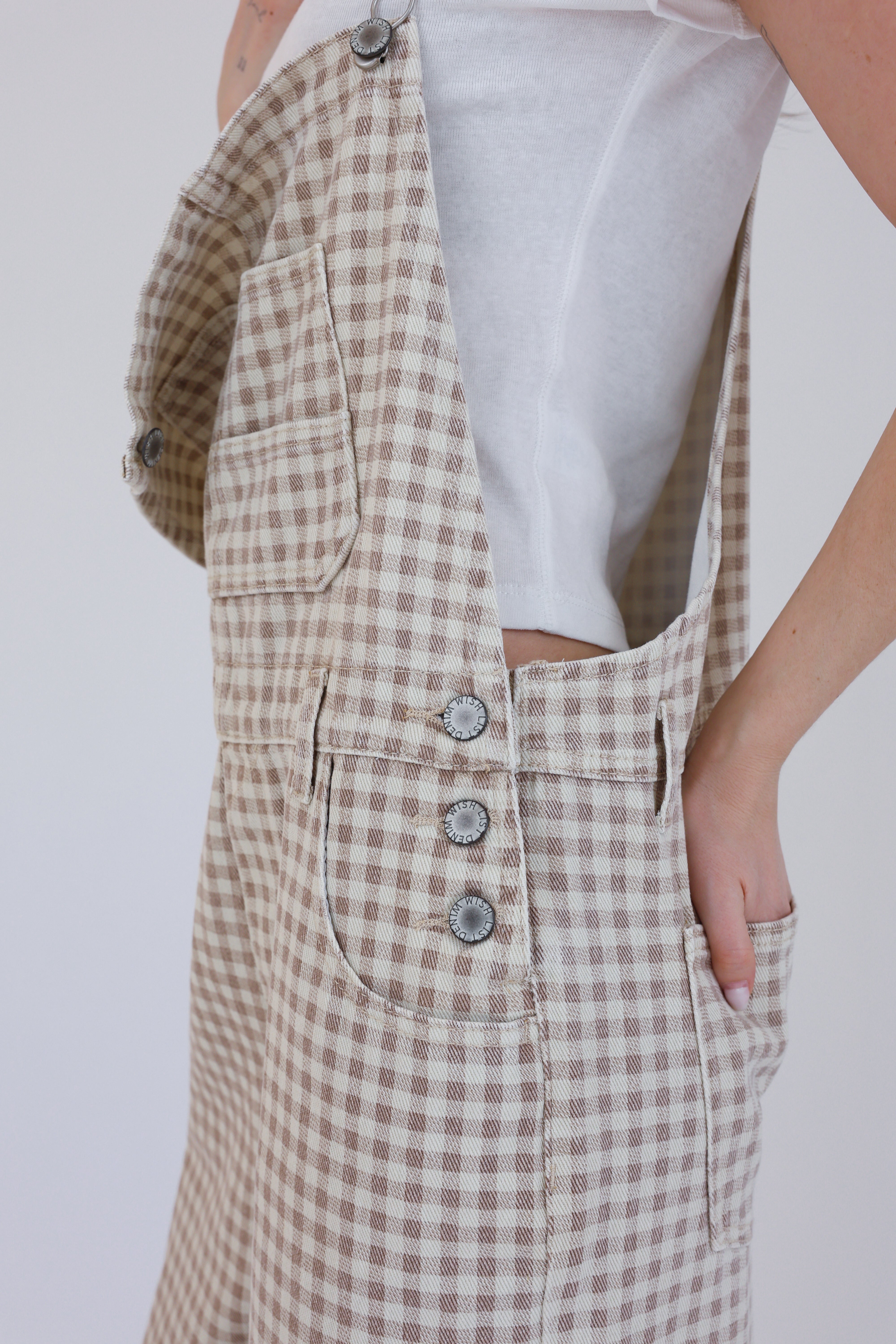 Person wearing a beige checkered dress with buttons on a white background