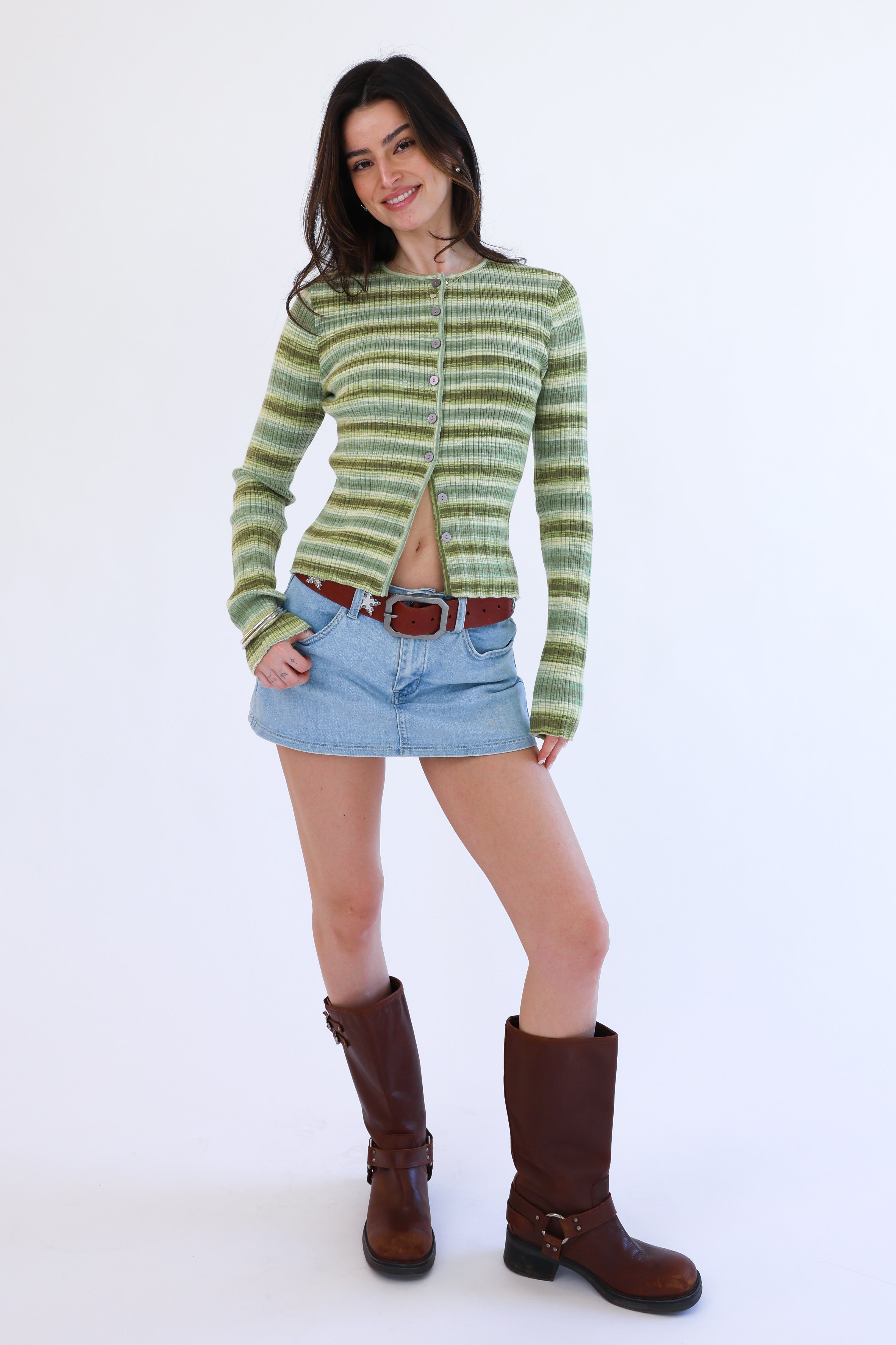 Woman wearing a green striped sweater, denim skirt, and brown boots on a white background