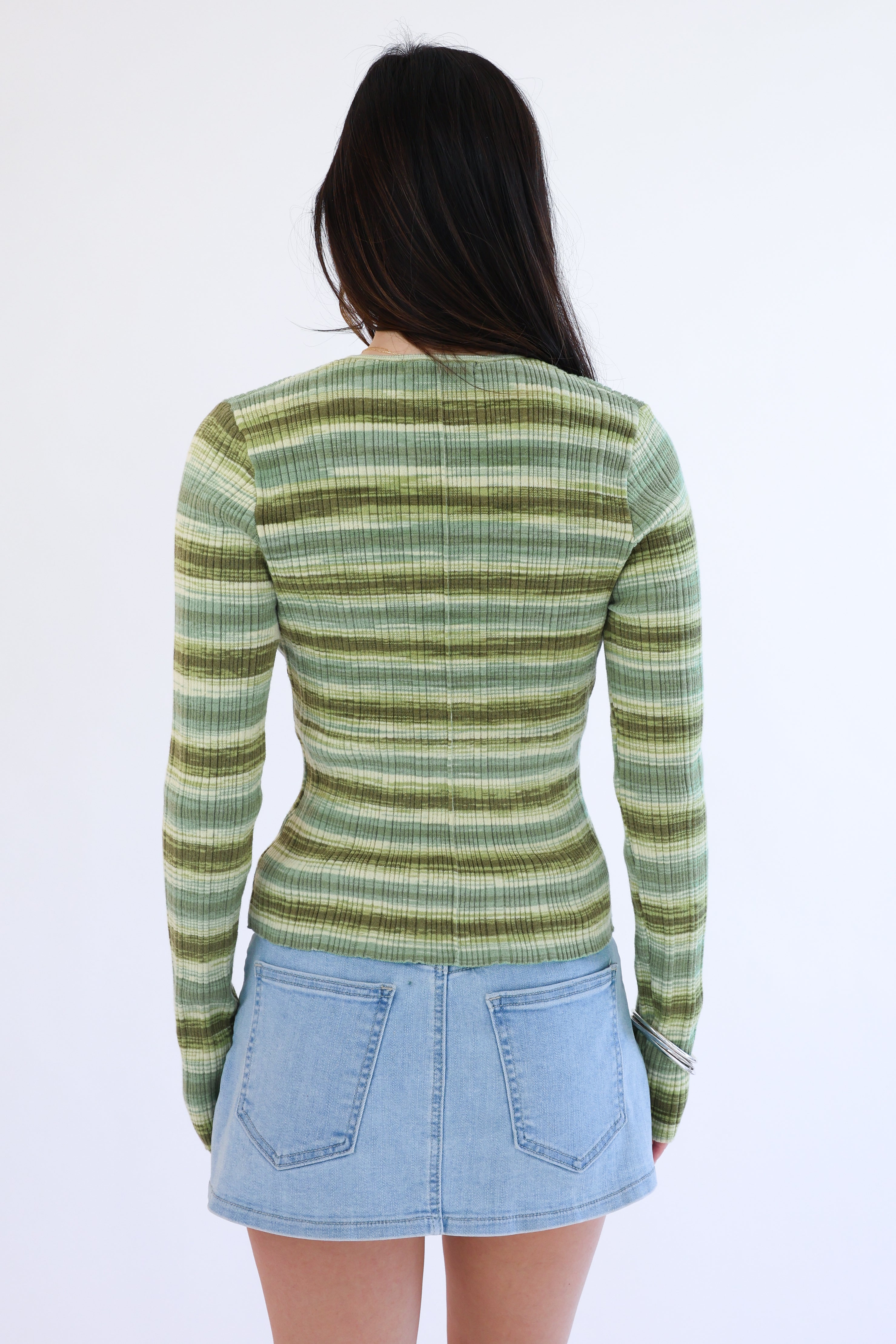 Person wearing a green striped sweater and denim skirt on a white background