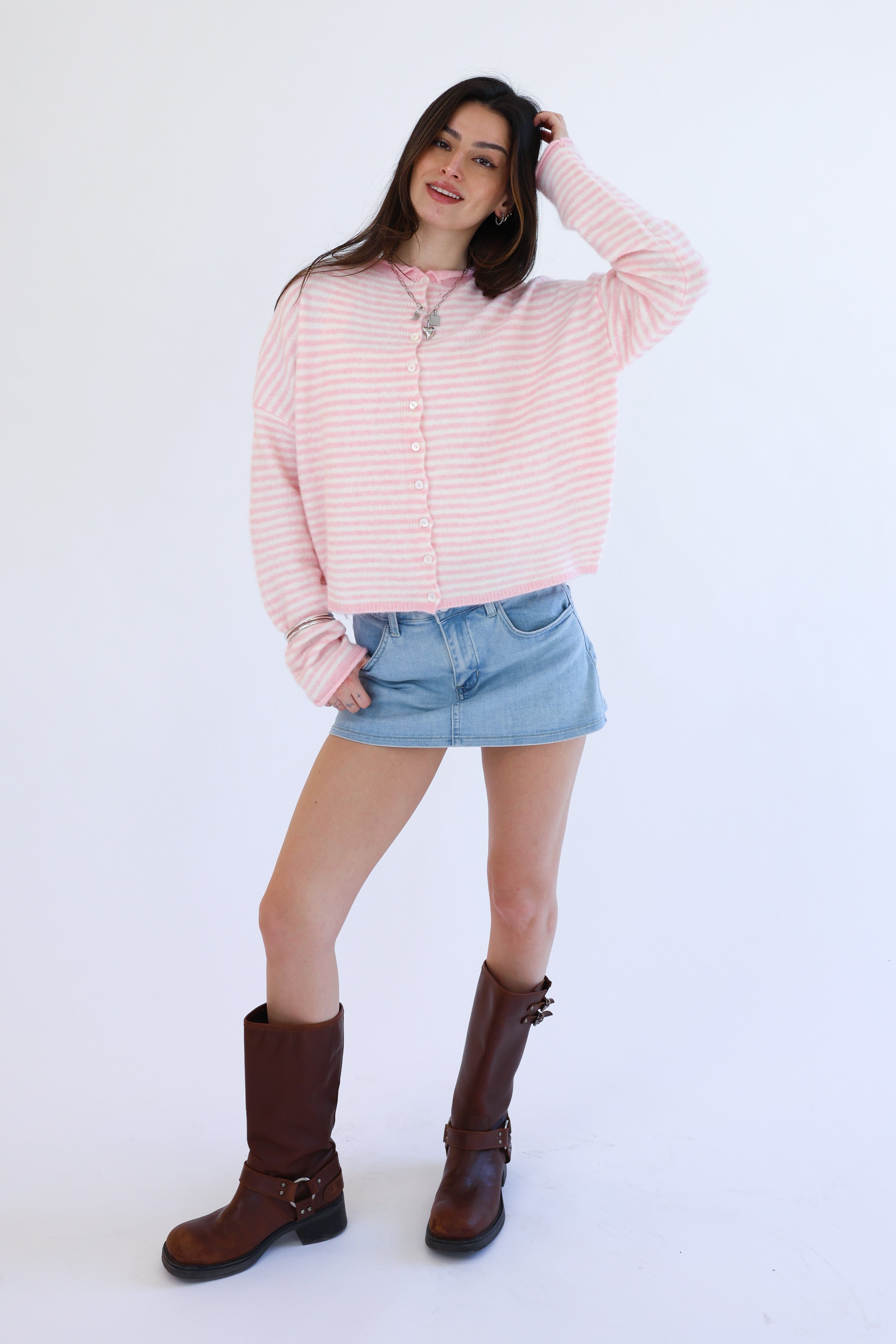 Woman wearing a pink striped shirt, denim skirt, and brown boots on a white background