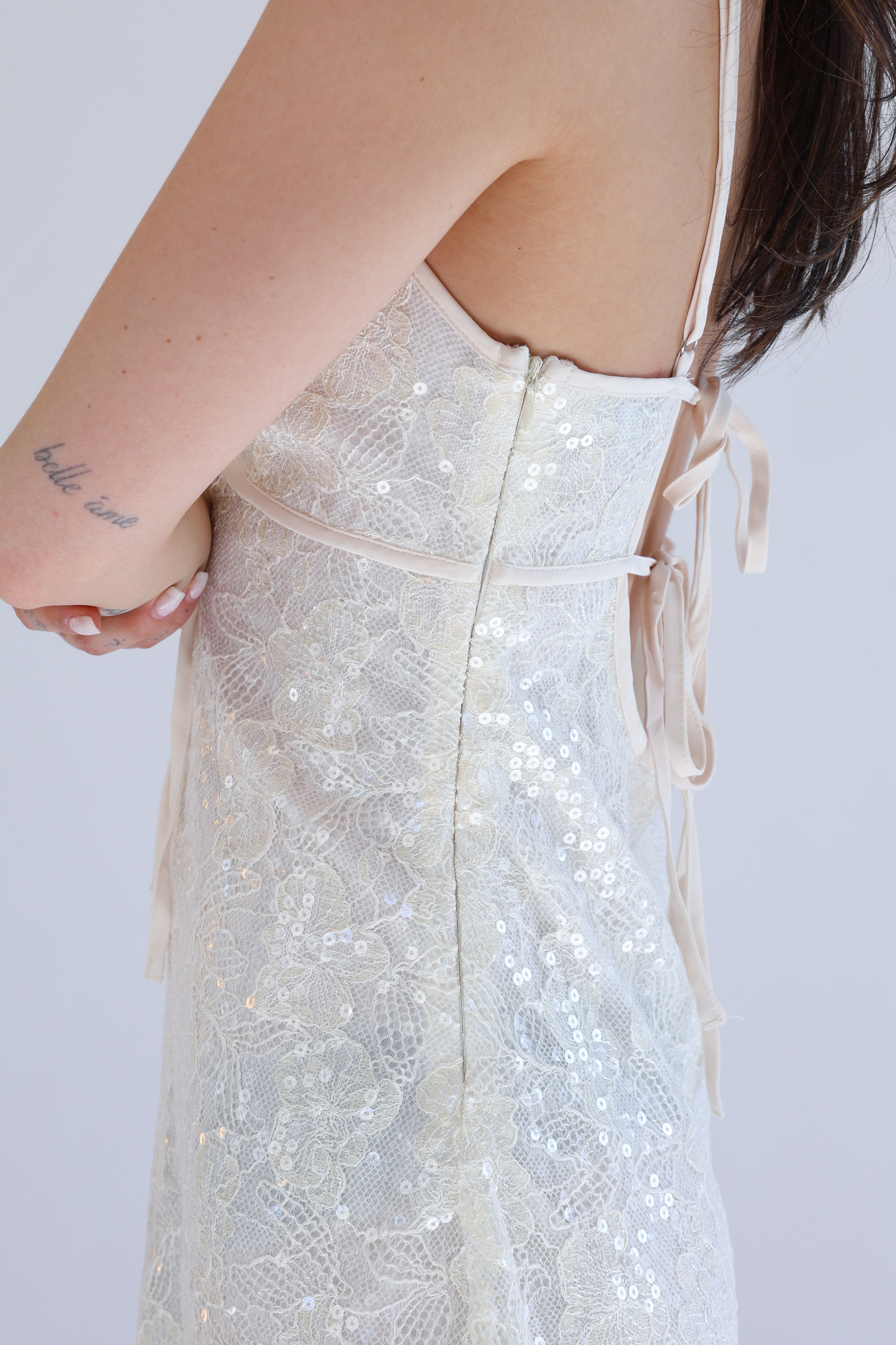 Close-up of a person wearing a sparkling white dress with a plain background