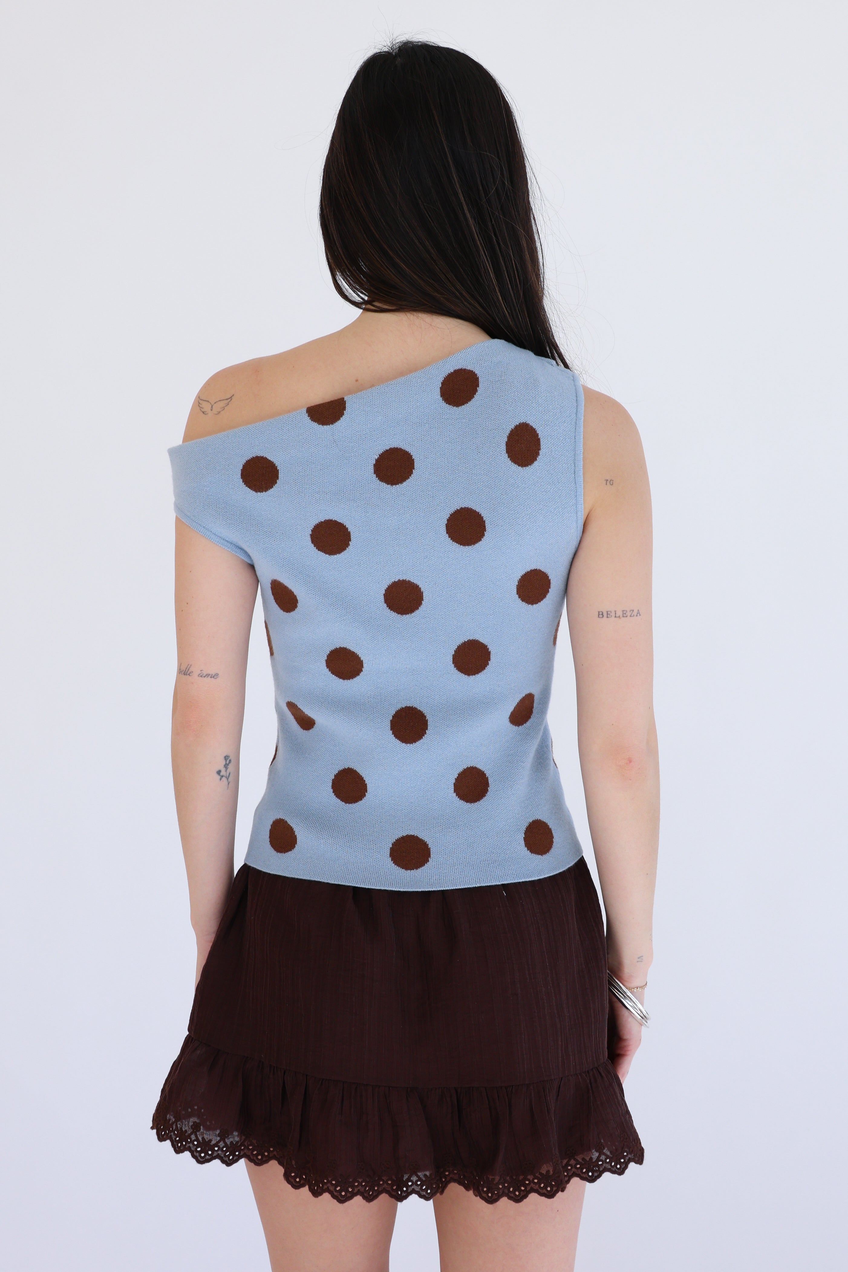 Person wearing a blue sleeveless top with brown polka dots and a brown skirt on a white background