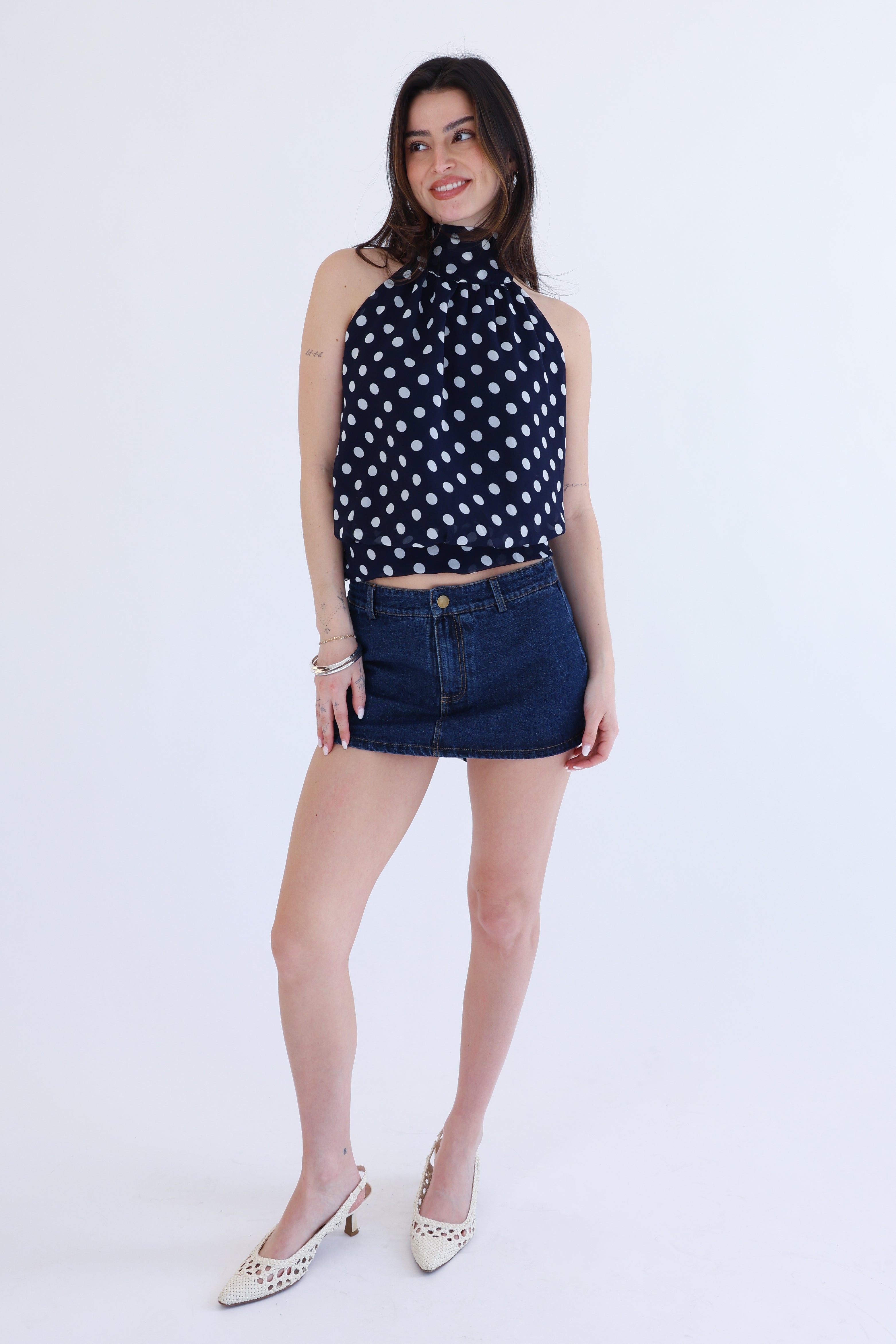 Woman wearing a polka dot top and denim skirt on a white background