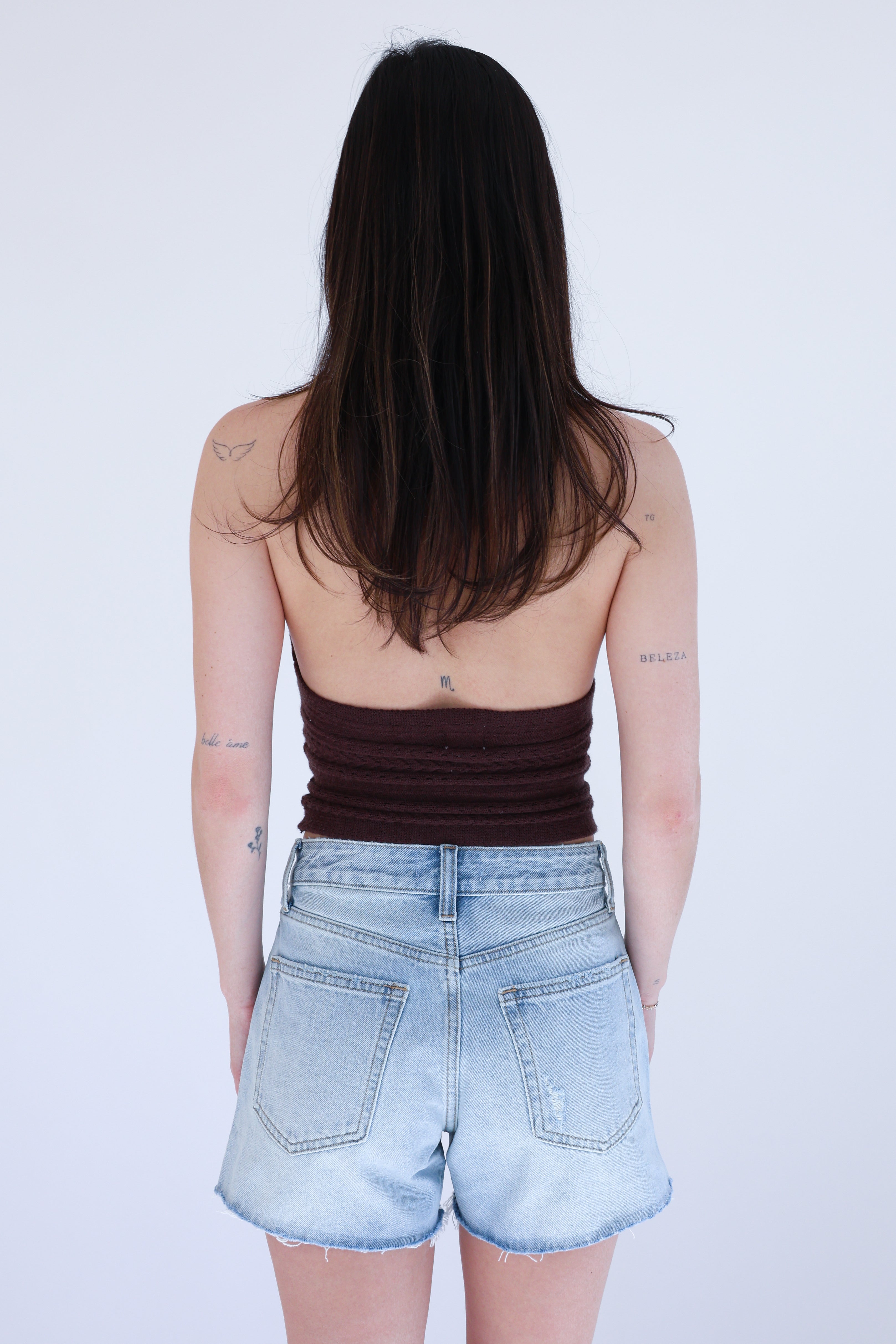 Person wearing a brown tank top and light blue denim shorts on a white background