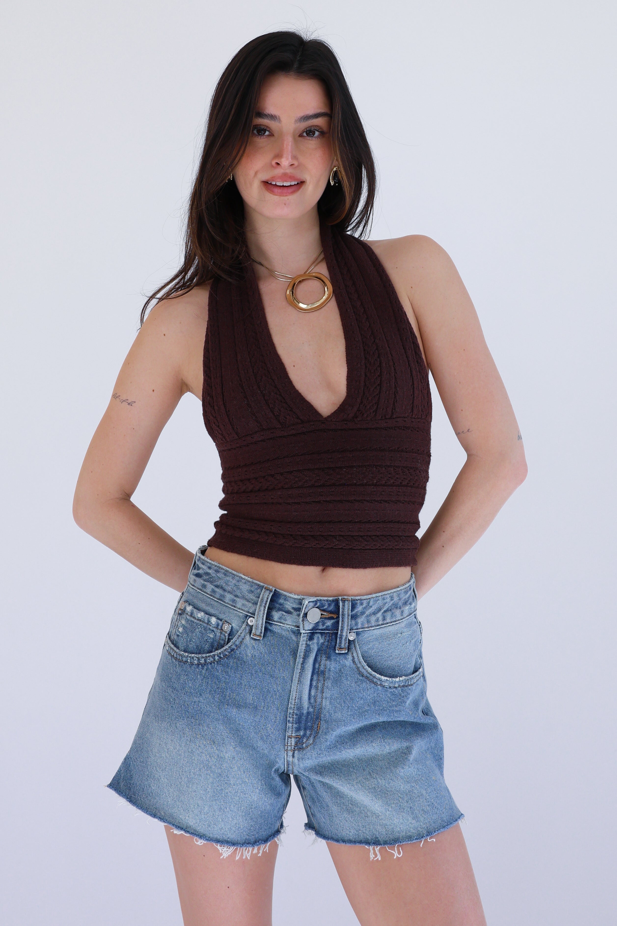 Woman wearing a brown halter top and blue denim shorts on a white background